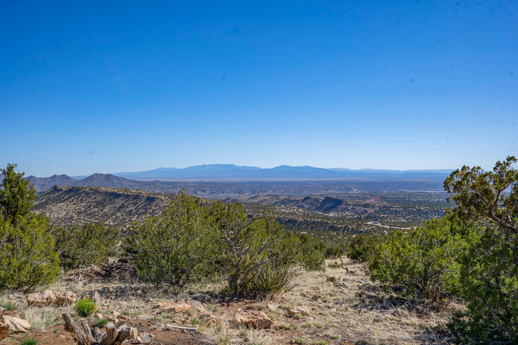 Mountain ranges and a wide valley viewed from a rocky, scrub-covered hillside.