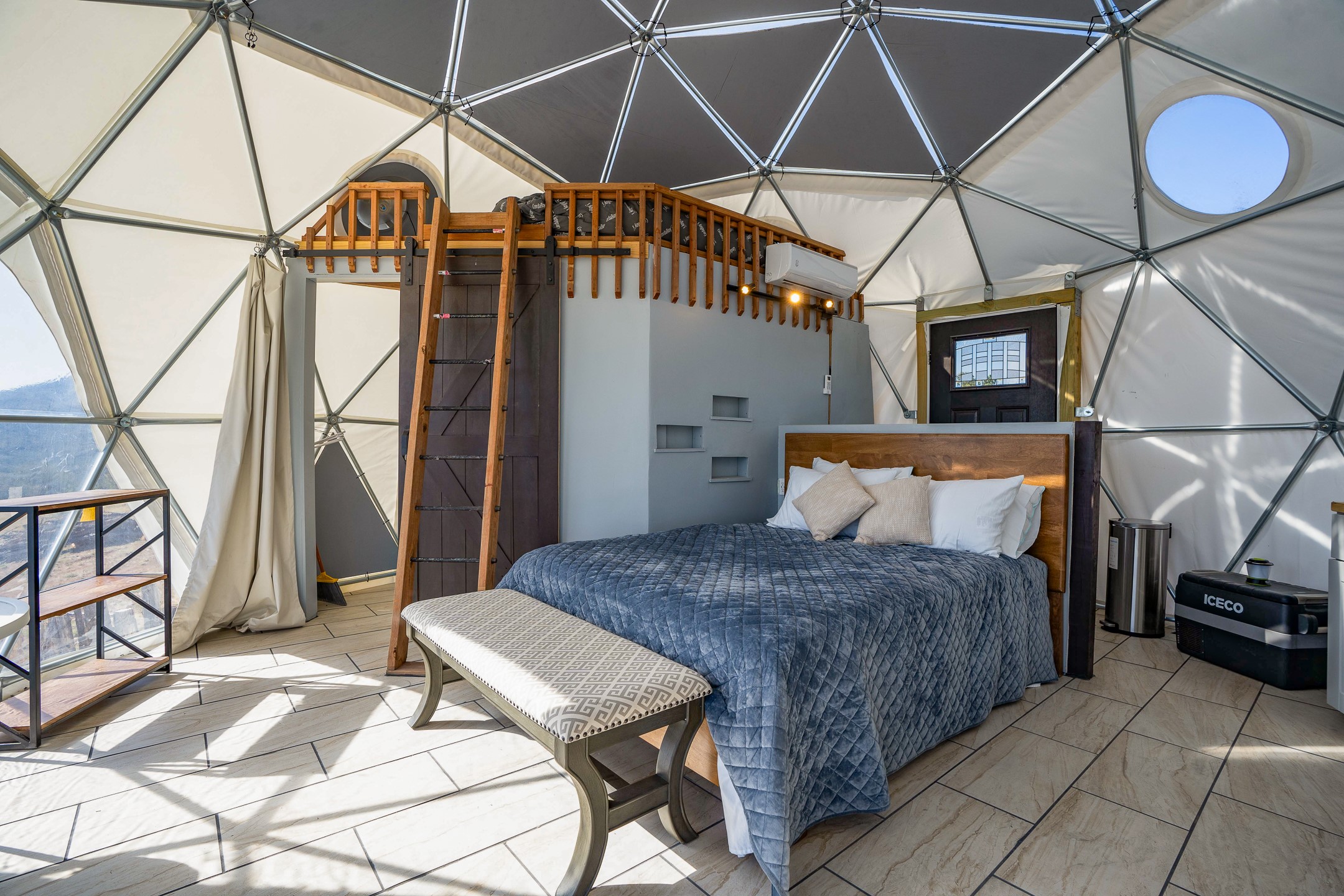 Dome bedroom with a king bed beneath a wooden loft and ladder.