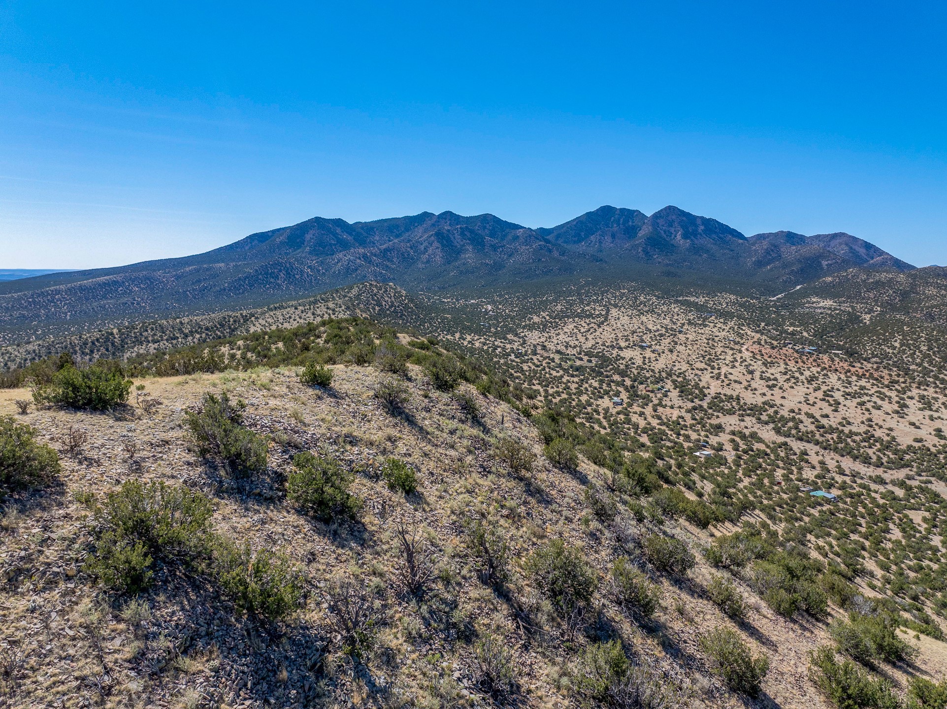 Rocky, shrub-covered vacant land overlooks a valley dotted with homes and a rugged mountain range.