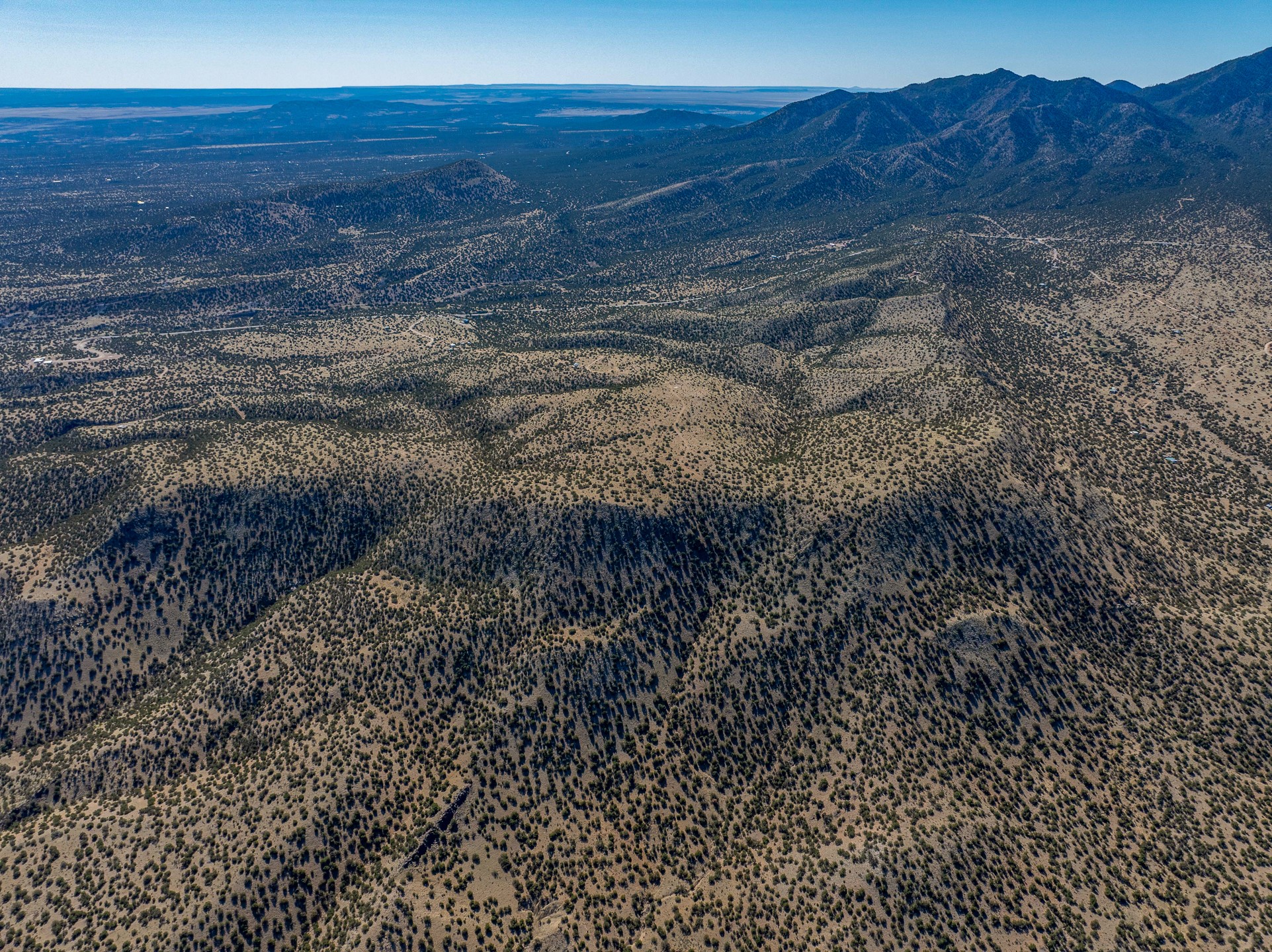 Aerial view of scrub-covered land and rolling hills with mountain ridges in the distance.