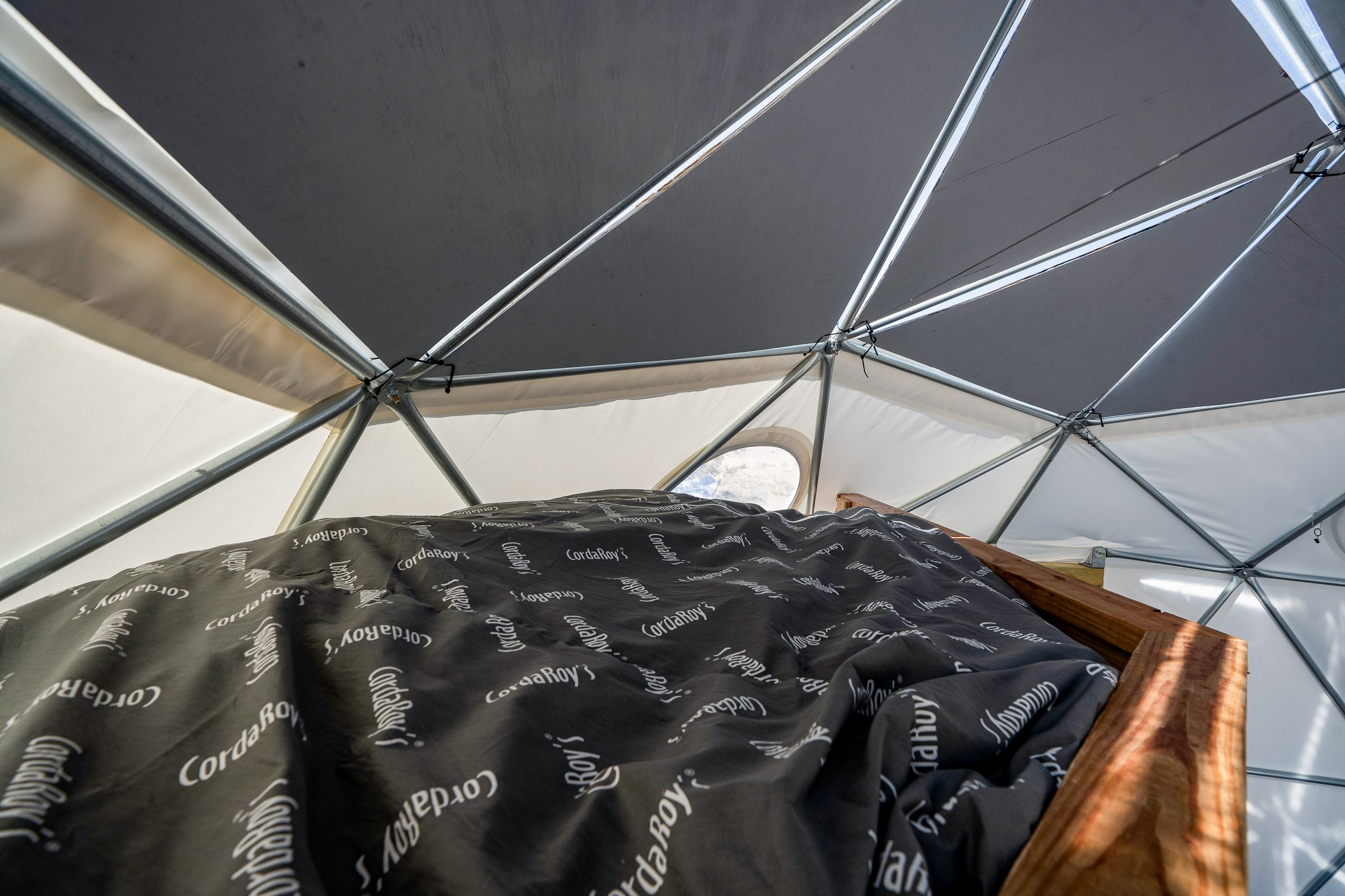 Bed with black CordaRoy's bedding inside a fabric-covered geodesic structure.