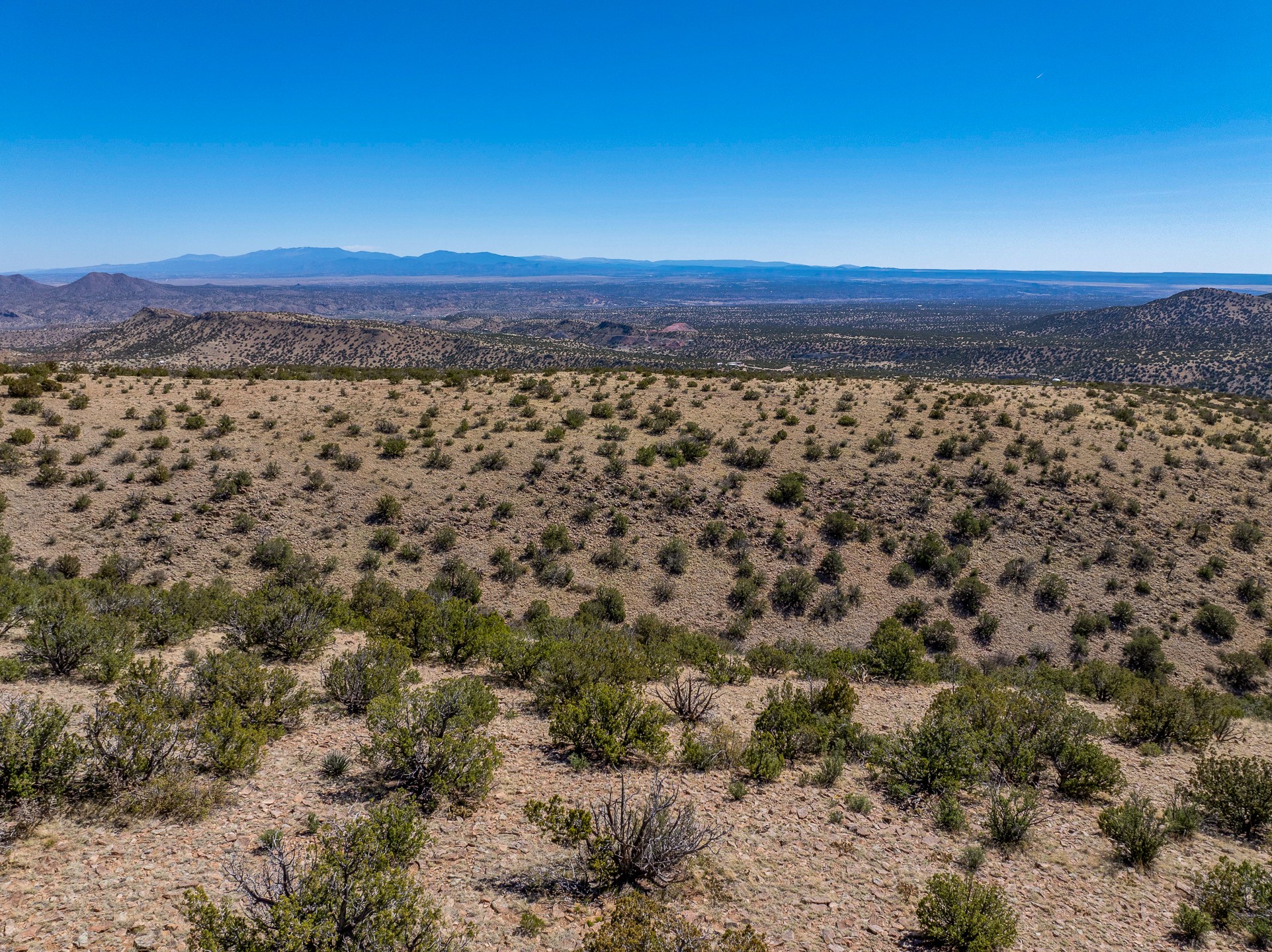 Vacant desert land with scattered shrubs and distant mountain views.