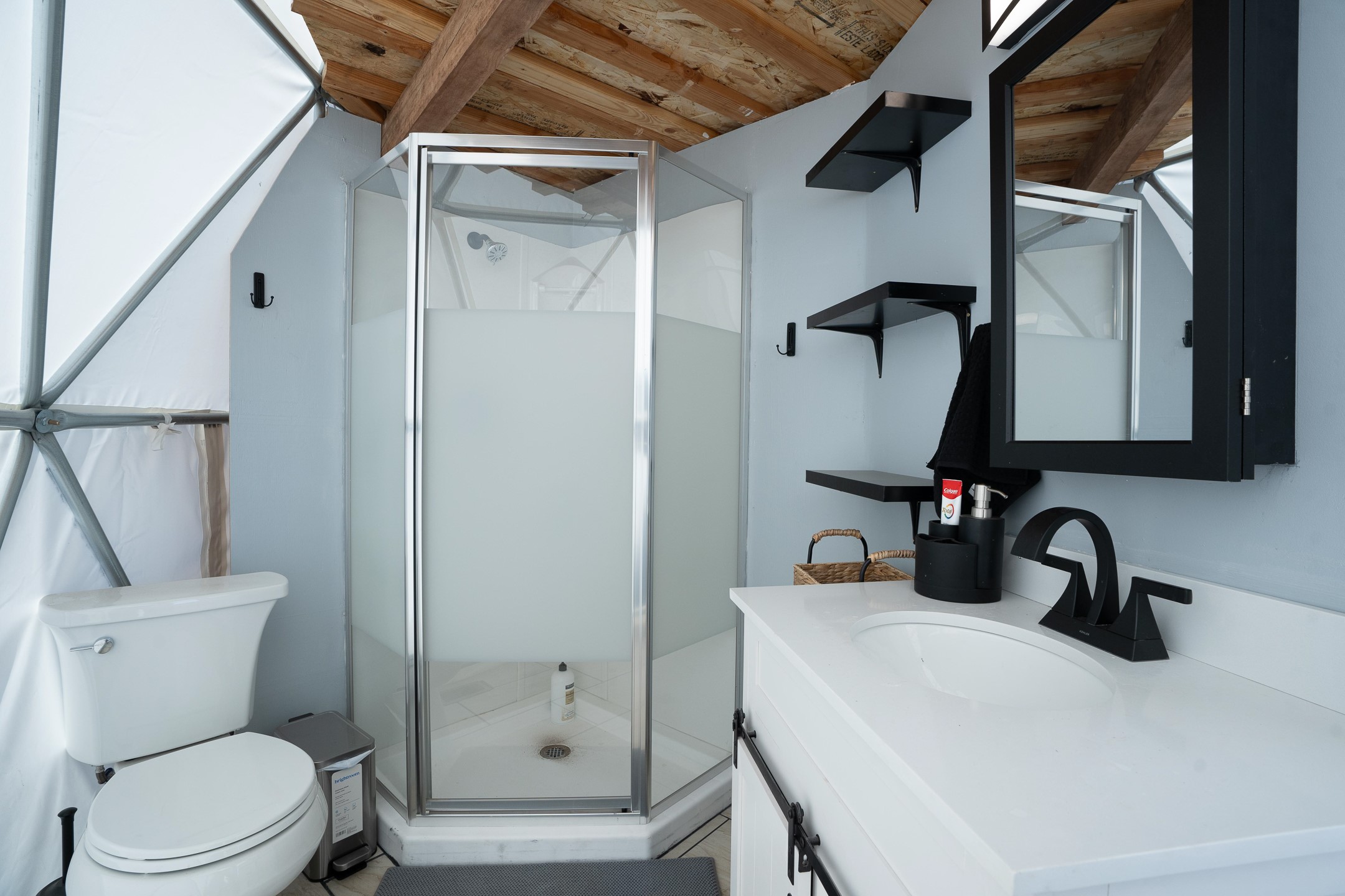 Bathroom with a glass corner shower, white vanity, black fixtures, and exposed wood ceiling.