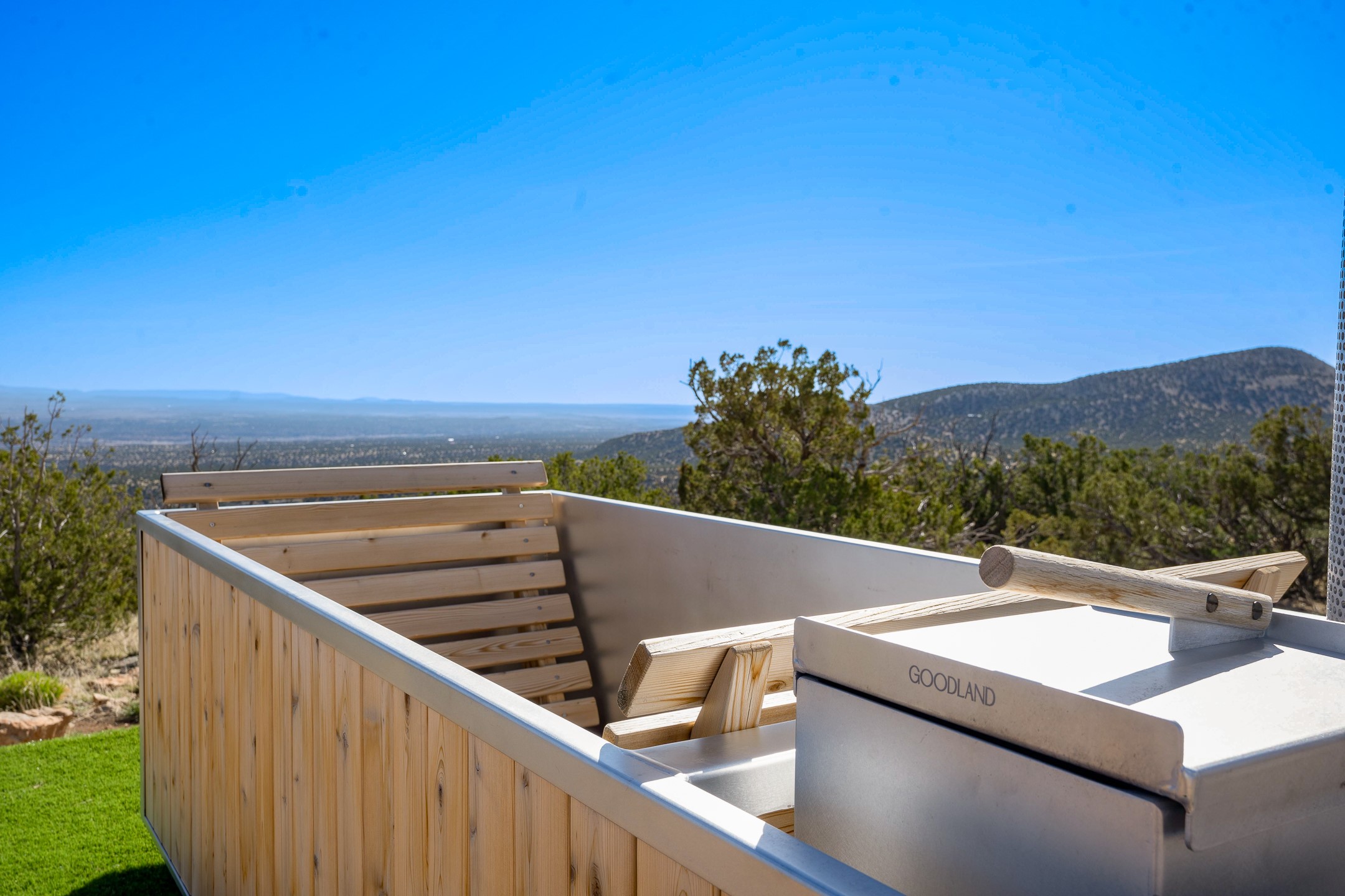 Outdoor wooden sauna with tiered benches and a wide view of the surrounding mountains.