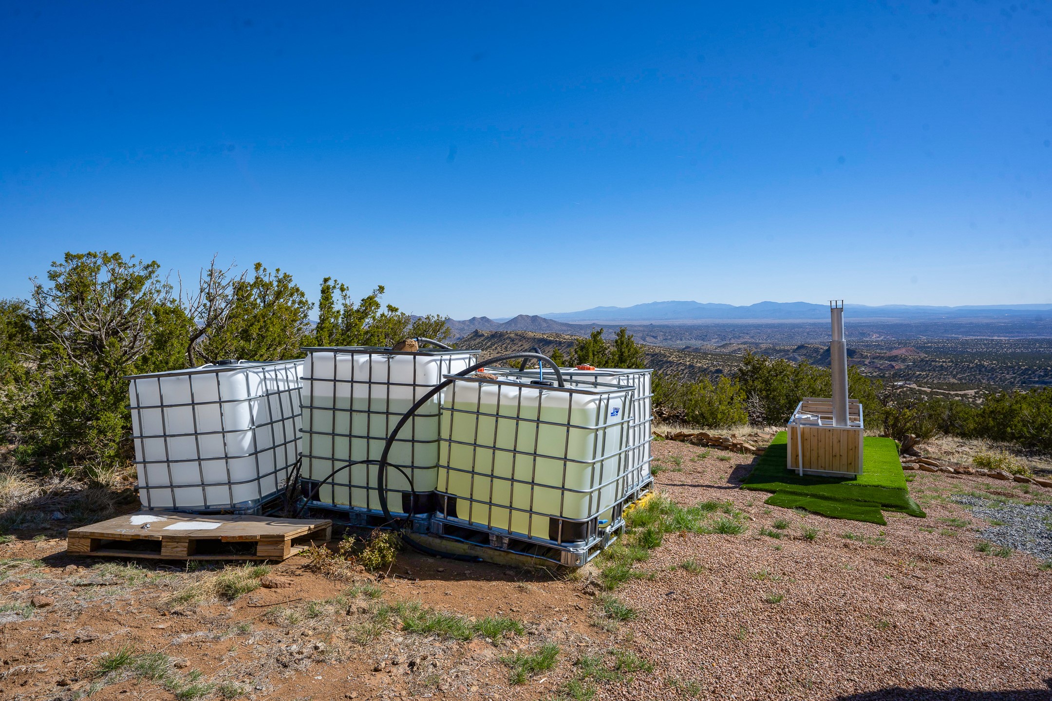 Water storage tanks and an outdoor unit on a gravel clearing, with distant mountain views.