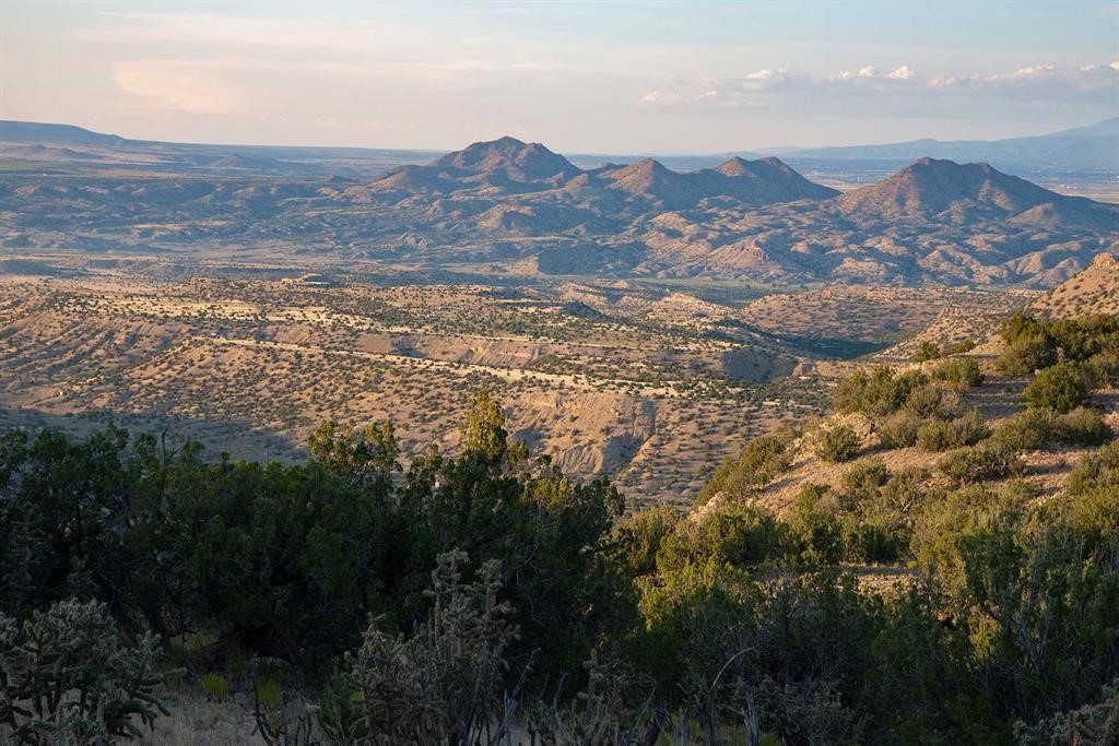 Panoramic New Mexico valley and rugged mountains beyond scrub-covered hills.