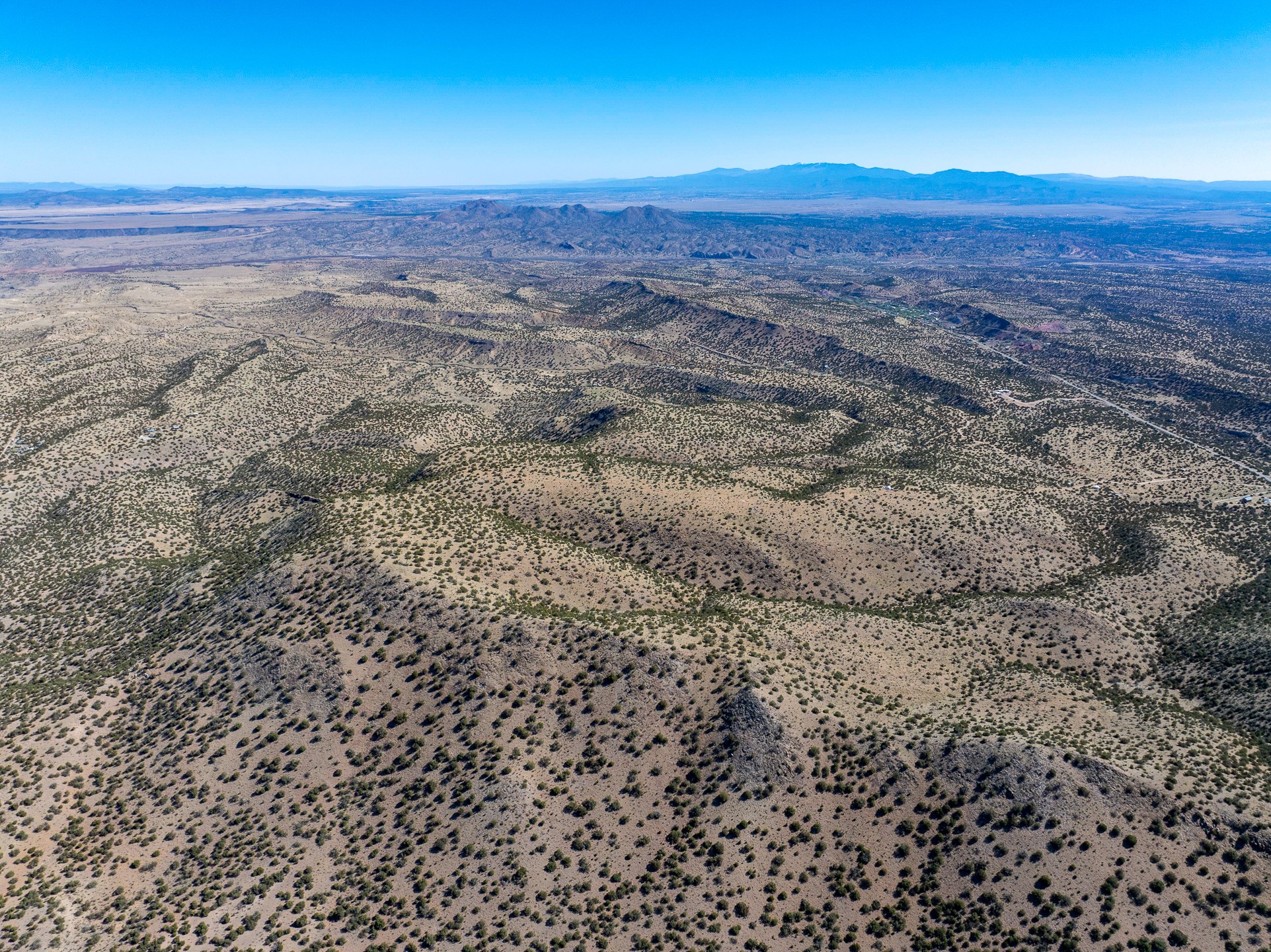 Aerial view of vacant desert land with rolling scrub-covered hills and distant mountains.