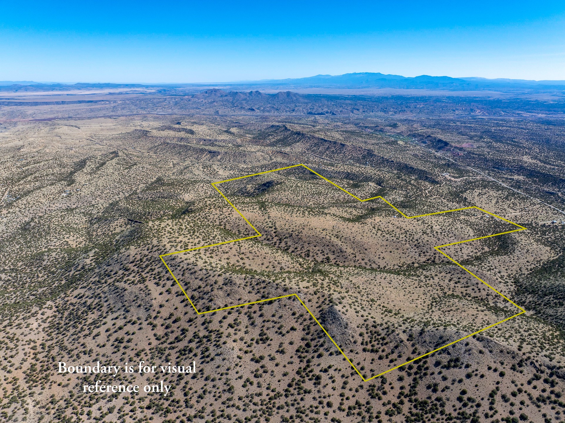 Aerial view of a sparsely vegetated desert parcel outlined in yellow, with distant mountains on the horizon.