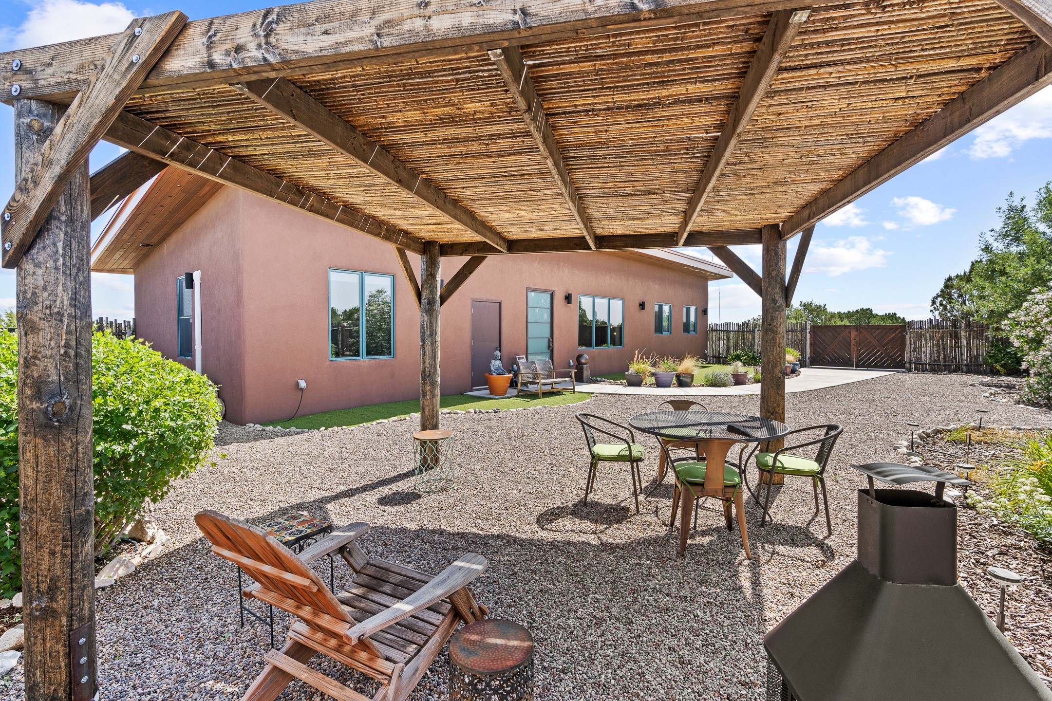 Home’s gravel patio beneath a timber pergola, furnished with lounge chairs, dining set, and chiminea.