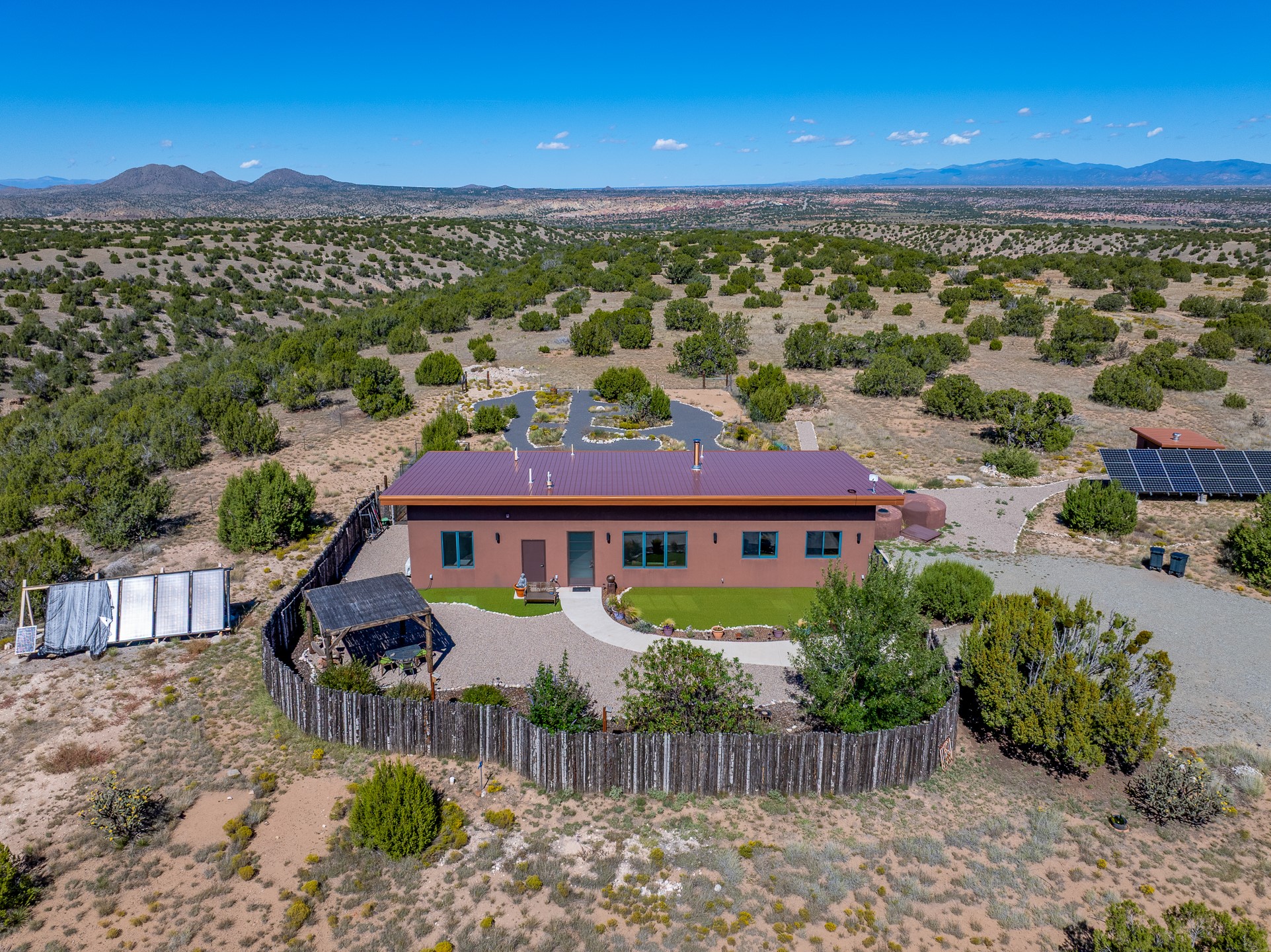 Aerial view of a single-story home with solar panels, a fenced yard, and distant mountain views.