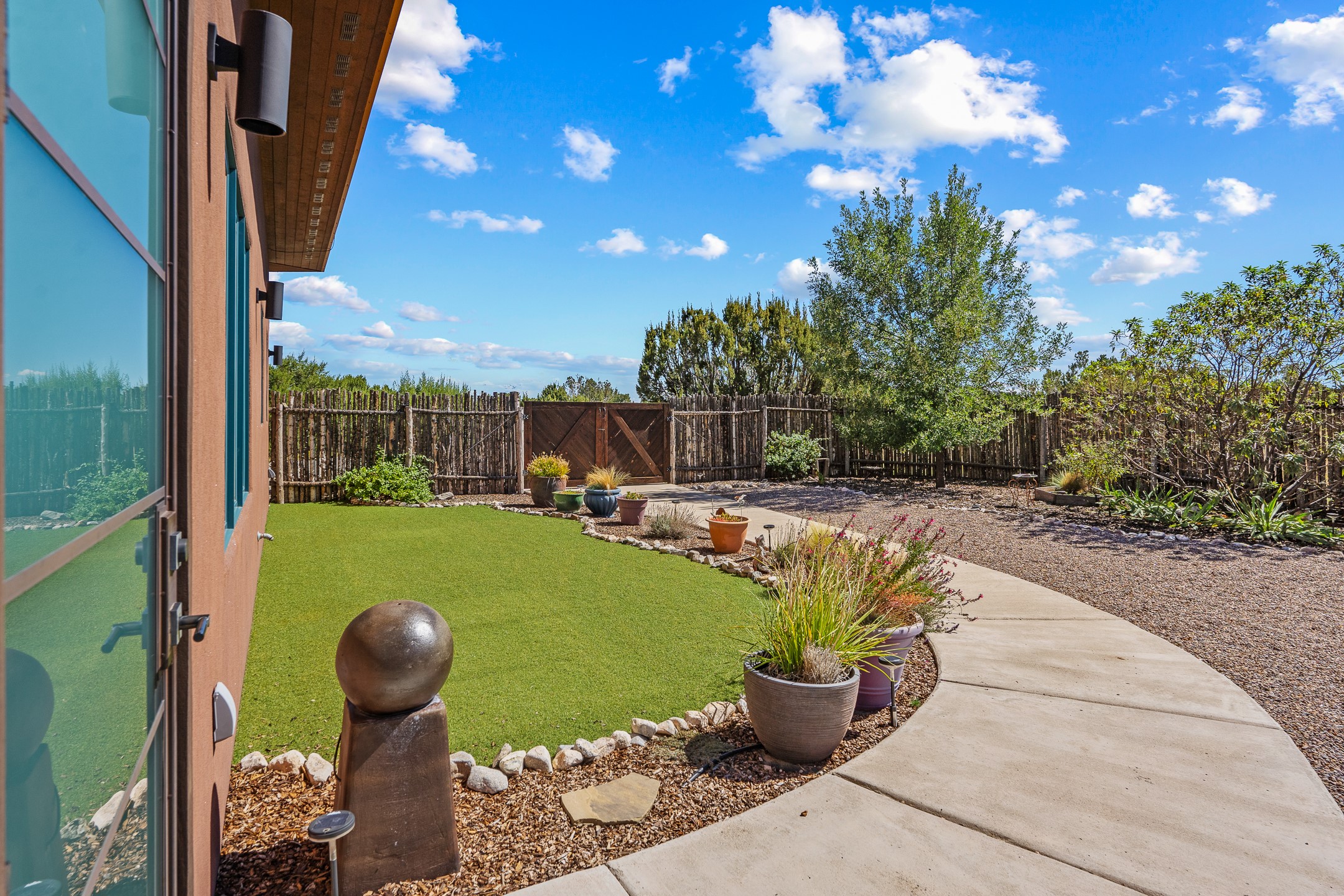 Backyard with artificial turf, a curved concrete walkway, potted plants, and a rustic wood fence.