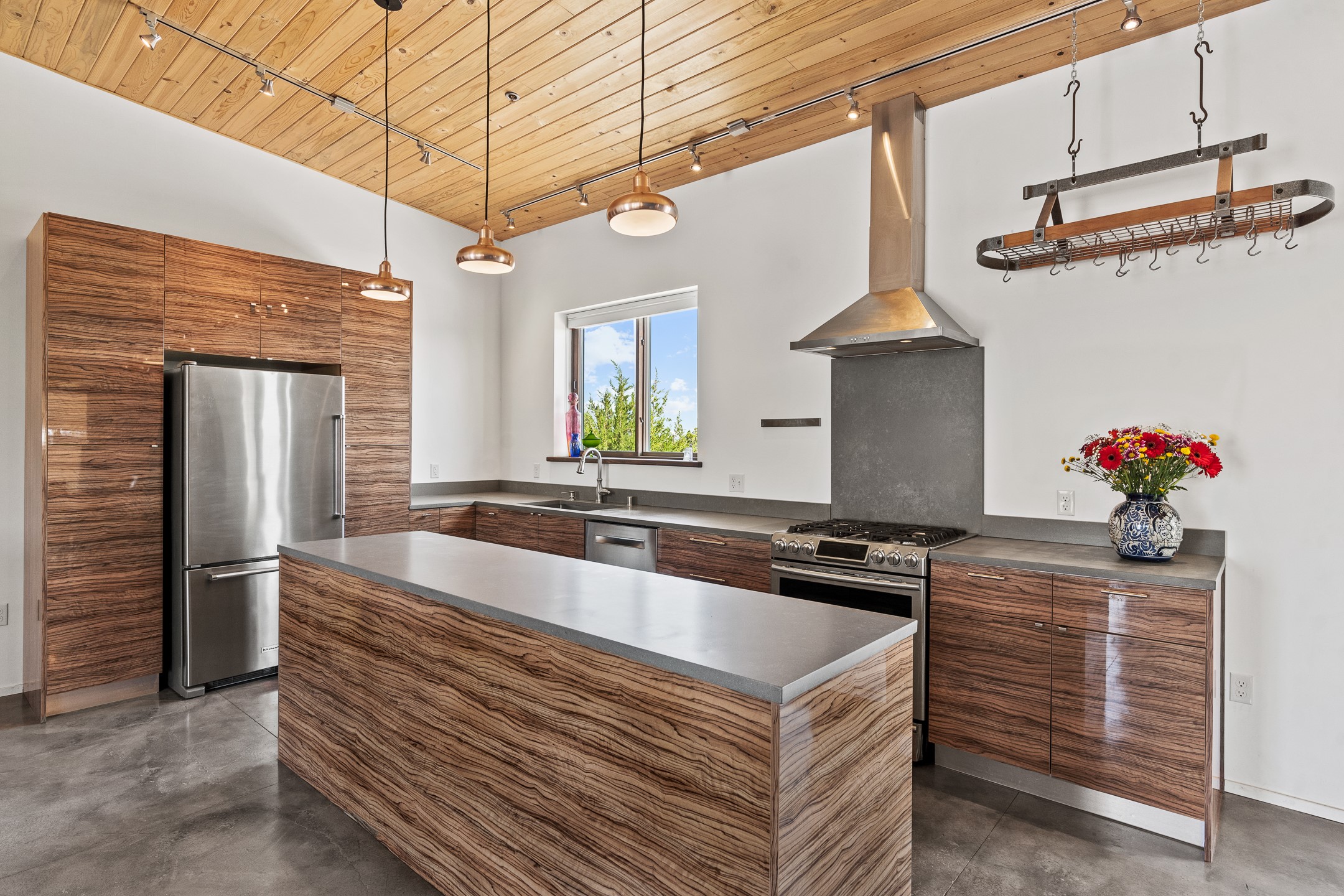 Modern kitchen with a wood-grain island, stainless steel appliances, and a wood-plank ceiling.