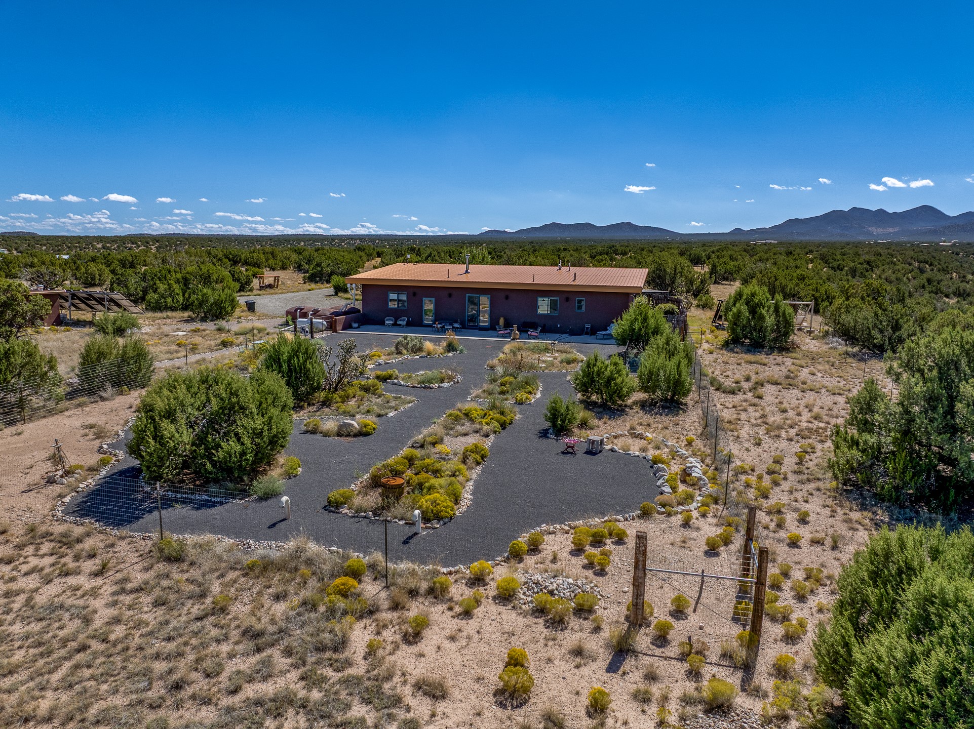 Aerial view of a single-story home with winding gravel paths and distant mountains.