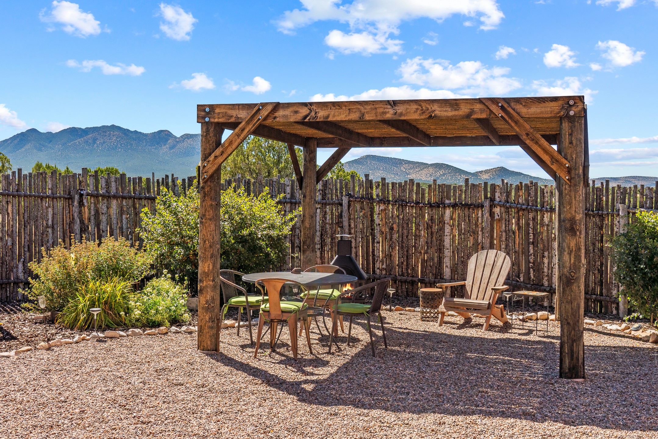 Gravel patio beneath a timber pergola, furnished for dining, with mountain views beyond the wooden fence.