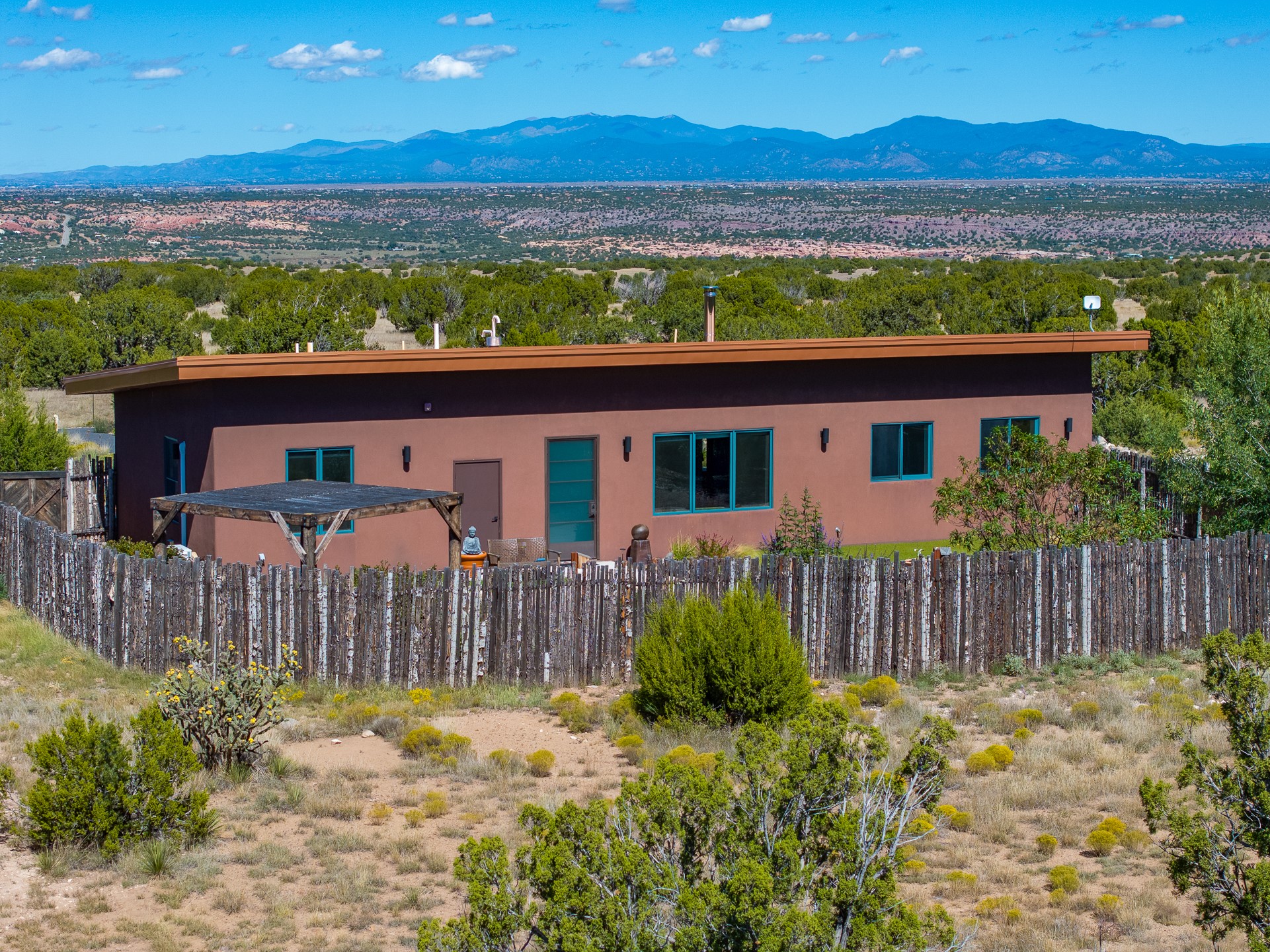 Single-story stucco home behind a rustic fence, with turquoise-trimmed windows and distant mountain views.