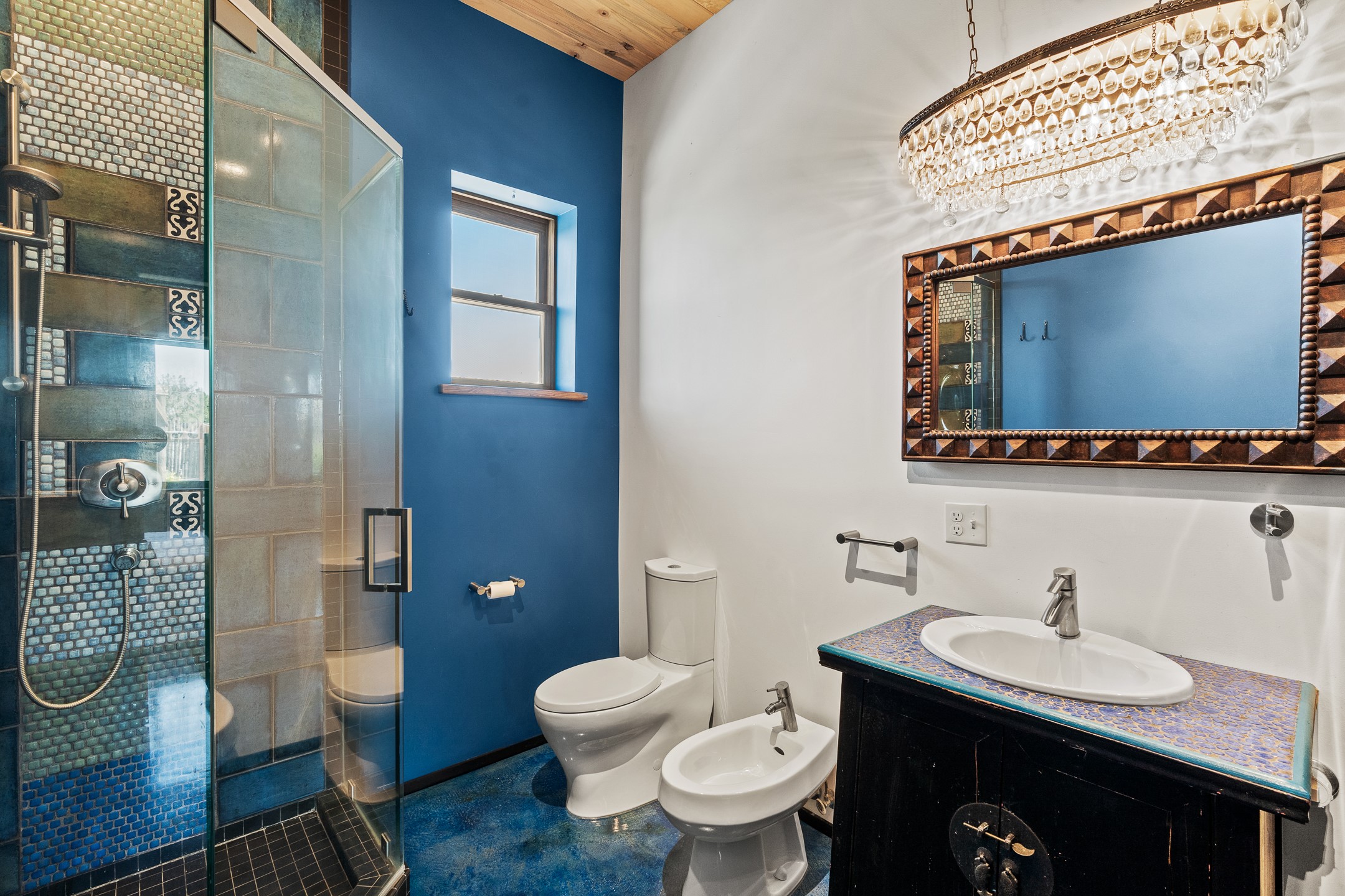 Bathroom with a blue mosaic-tile shower, colorful vanity countertop, and crystal chandelier.