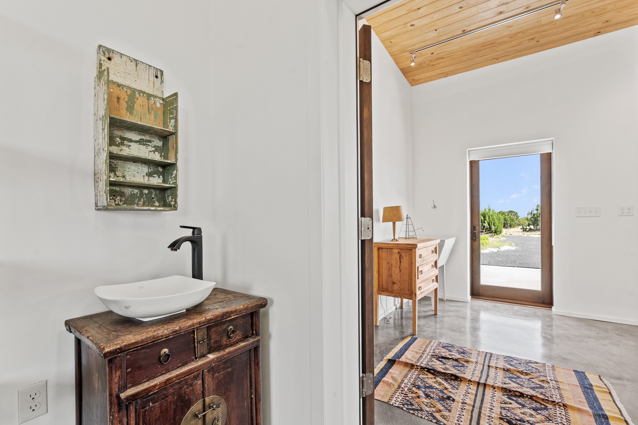 Bathroom vanity with a vessel sink and weathered wood details, looking through an open door to the entryway.