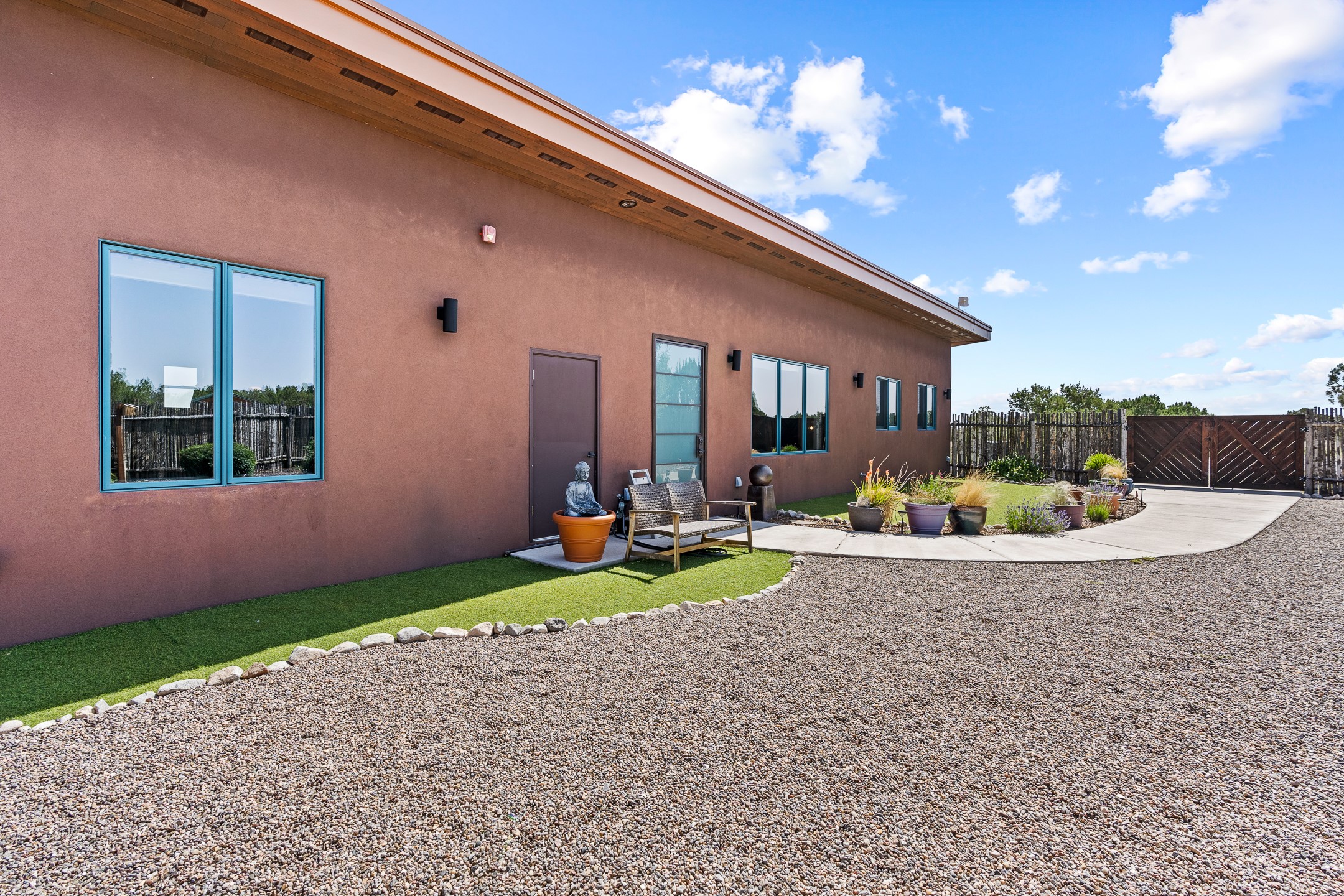 Brown stucco home with blue-trimmed windows, gravel yard, patio seating, and potted plants.