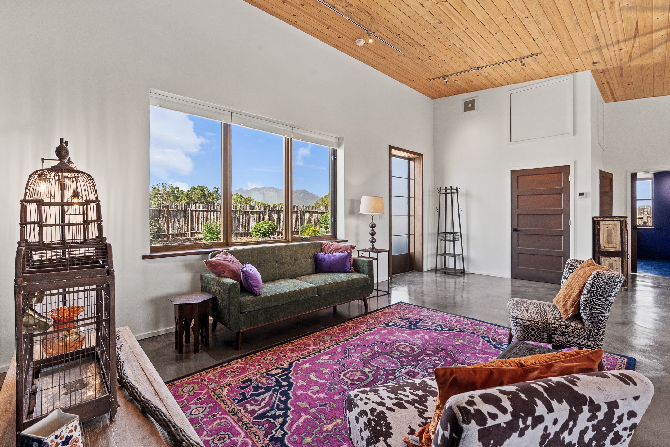 Living room with a wood ceiling, colorful rug, and windows overlooking distant mountains.