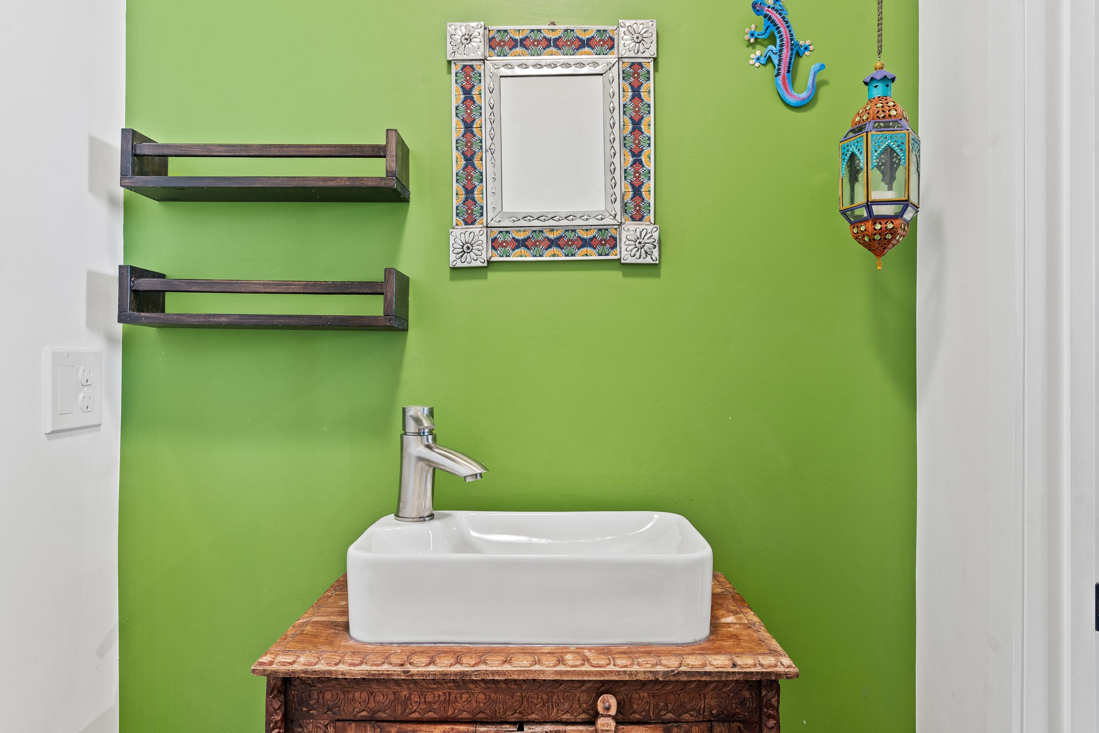 Bathroom vanity with a white vessel sink, carved wooden counter, and colorful decorations on a bright green wall.