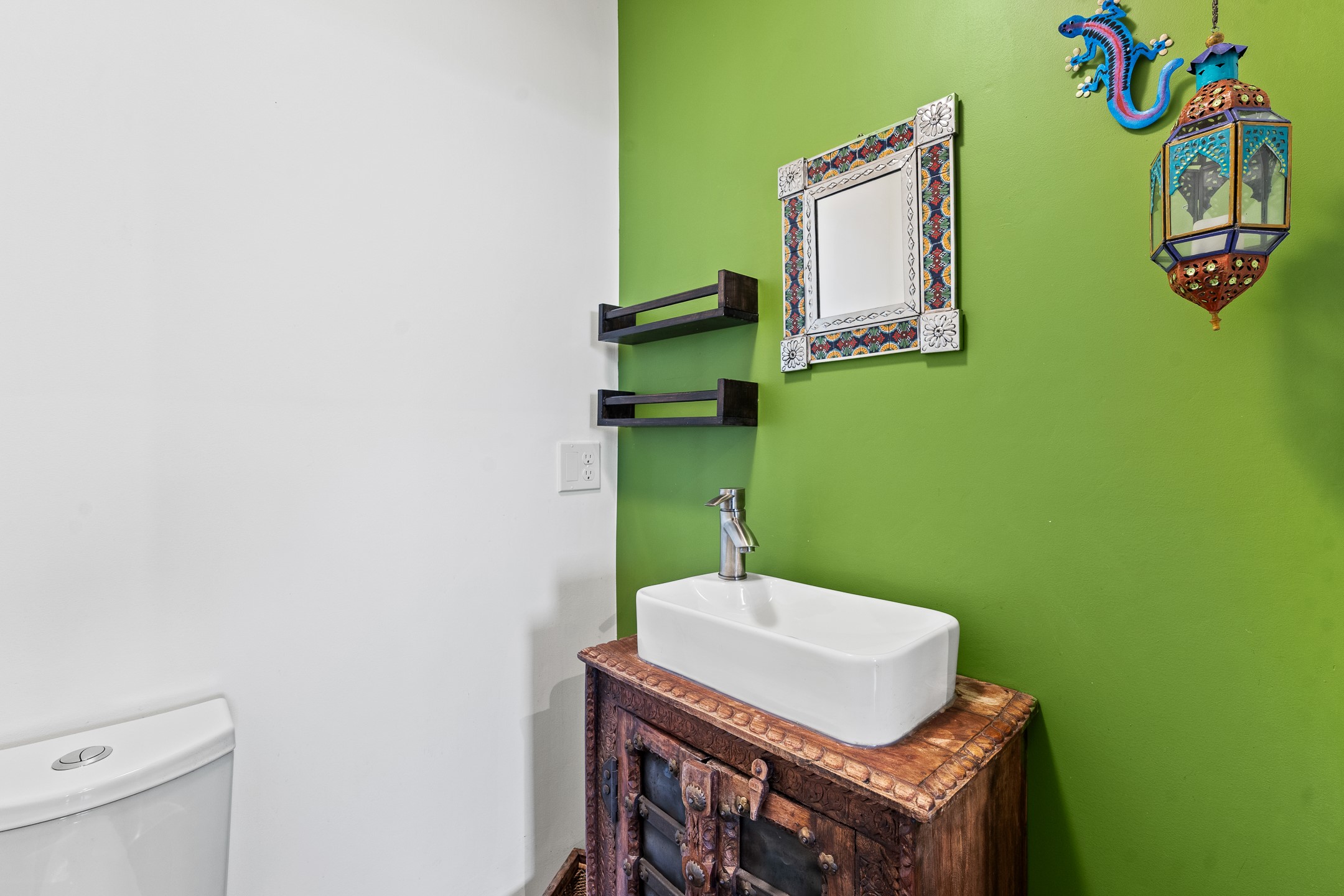 Bathroom with a white vessel sink on a carved wooden vanity against a bright green wall.