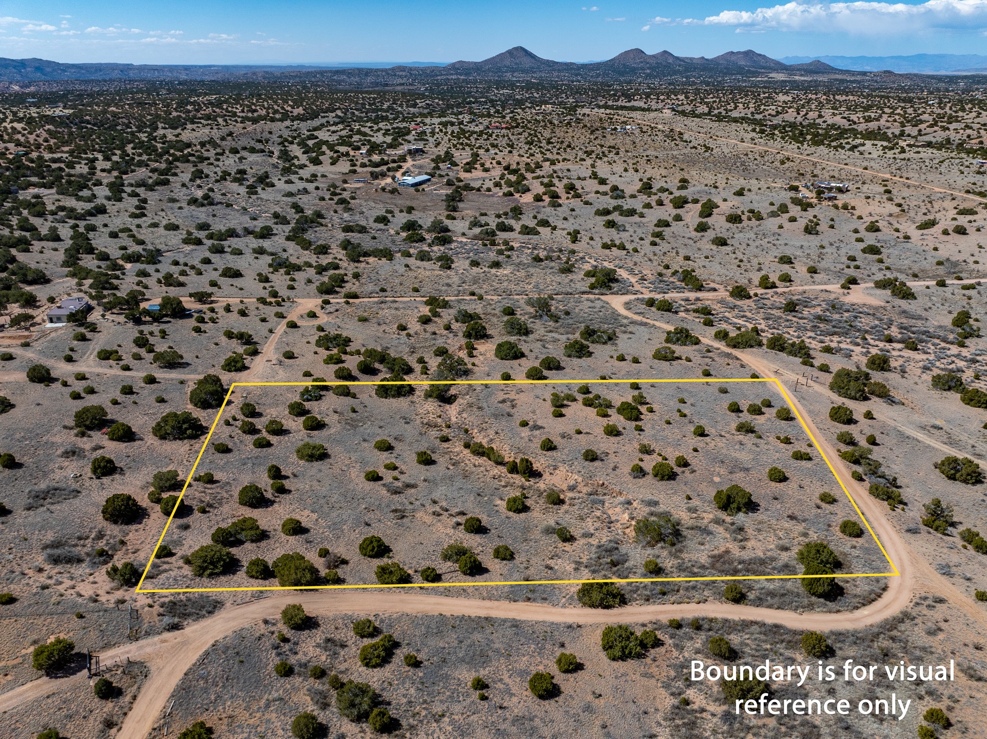 Aerial view of scrubland parcel outlined in yellow, with dirt roads and distant mountains.