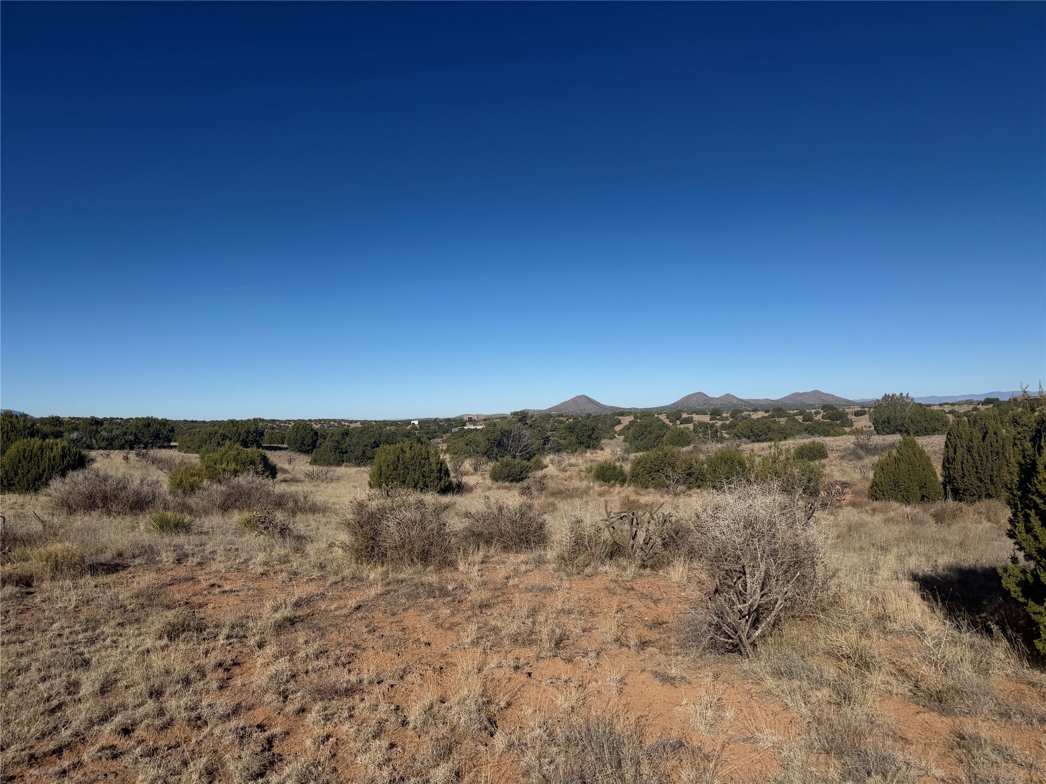 Vacant scrubland parcel with juniper bushes, reddish earth, and distant mountains.