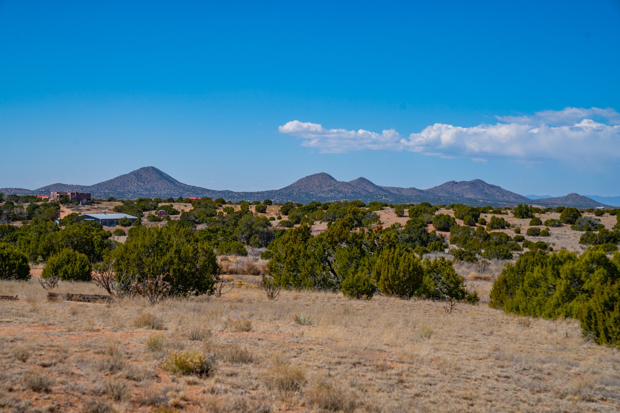 Vacant high-desert land with scattered shrubs and distant mountains under a blue sky.