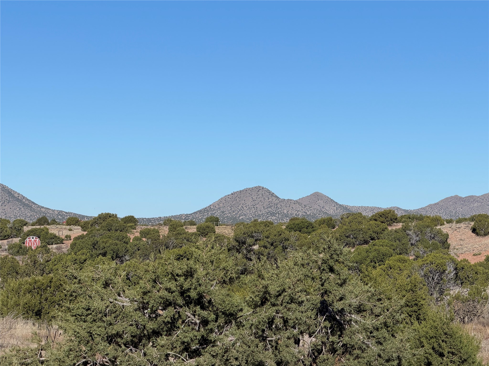 Mountain views across wooded high-desert terrain, with a small red barn at left.