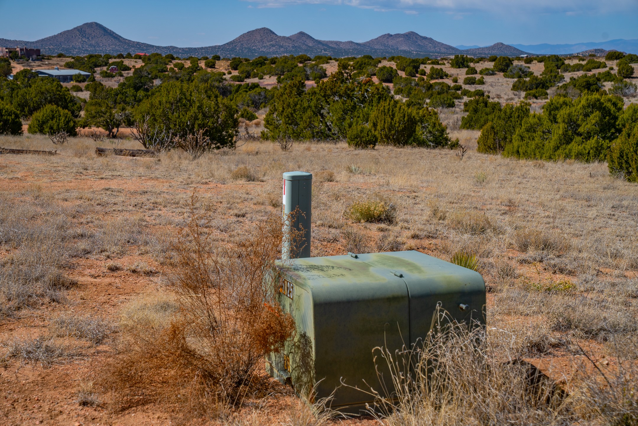 High-desert parcel with foreground utility enclosures, scattered scrub, and distant mountains.
