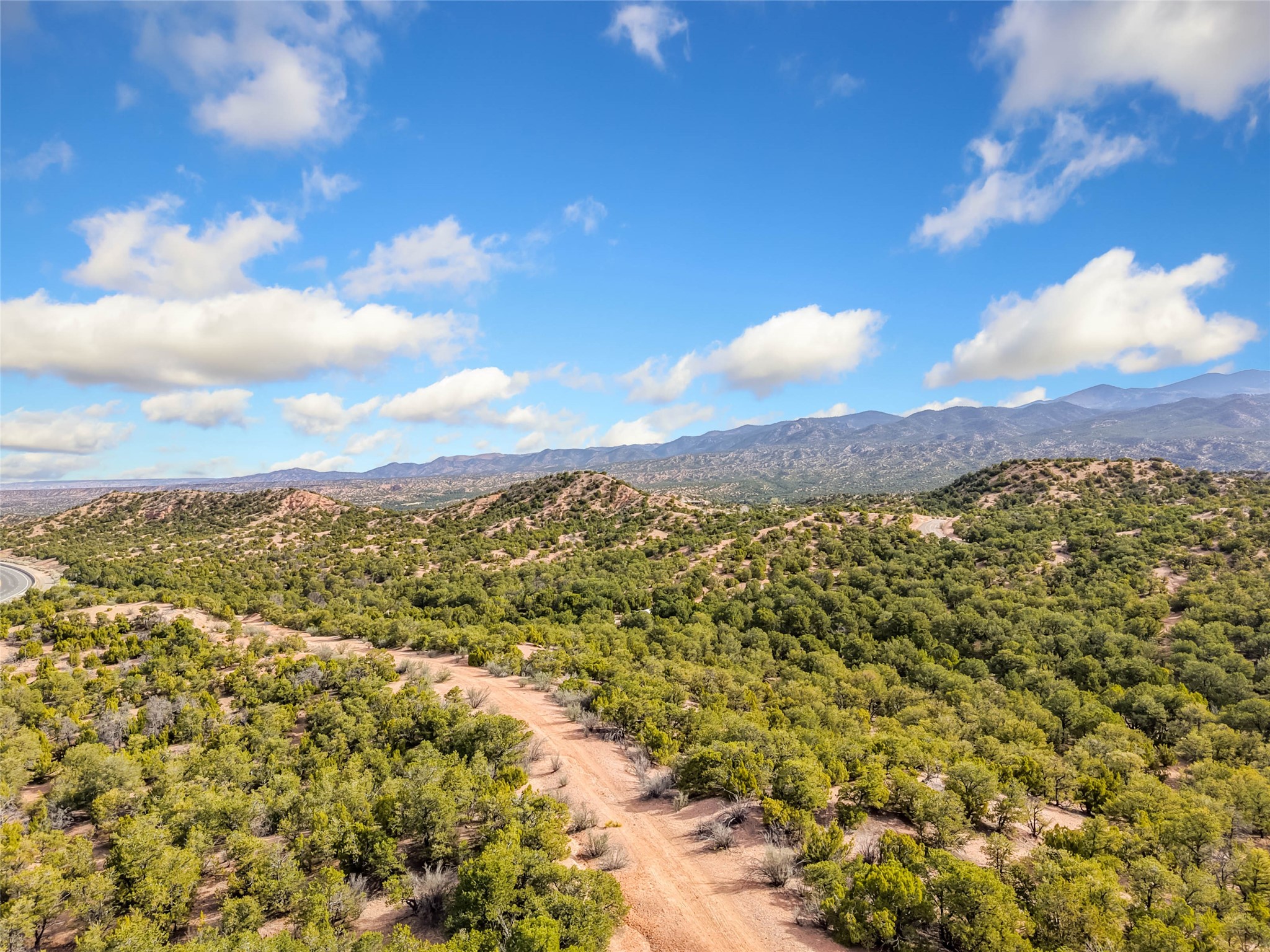 Aerial view of scrub-covered acreage with a winding dirt road and distant mountain ranges.