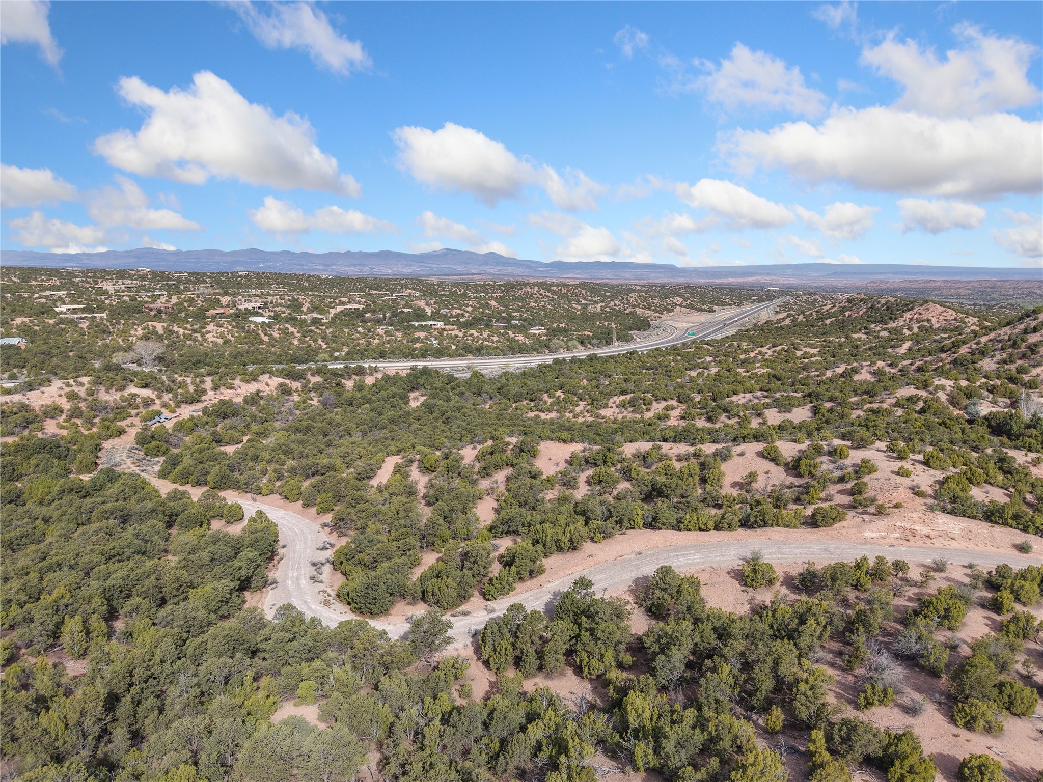 Aerial view of scrub-covered vacant land, with winding dirt roads and distant mountains.