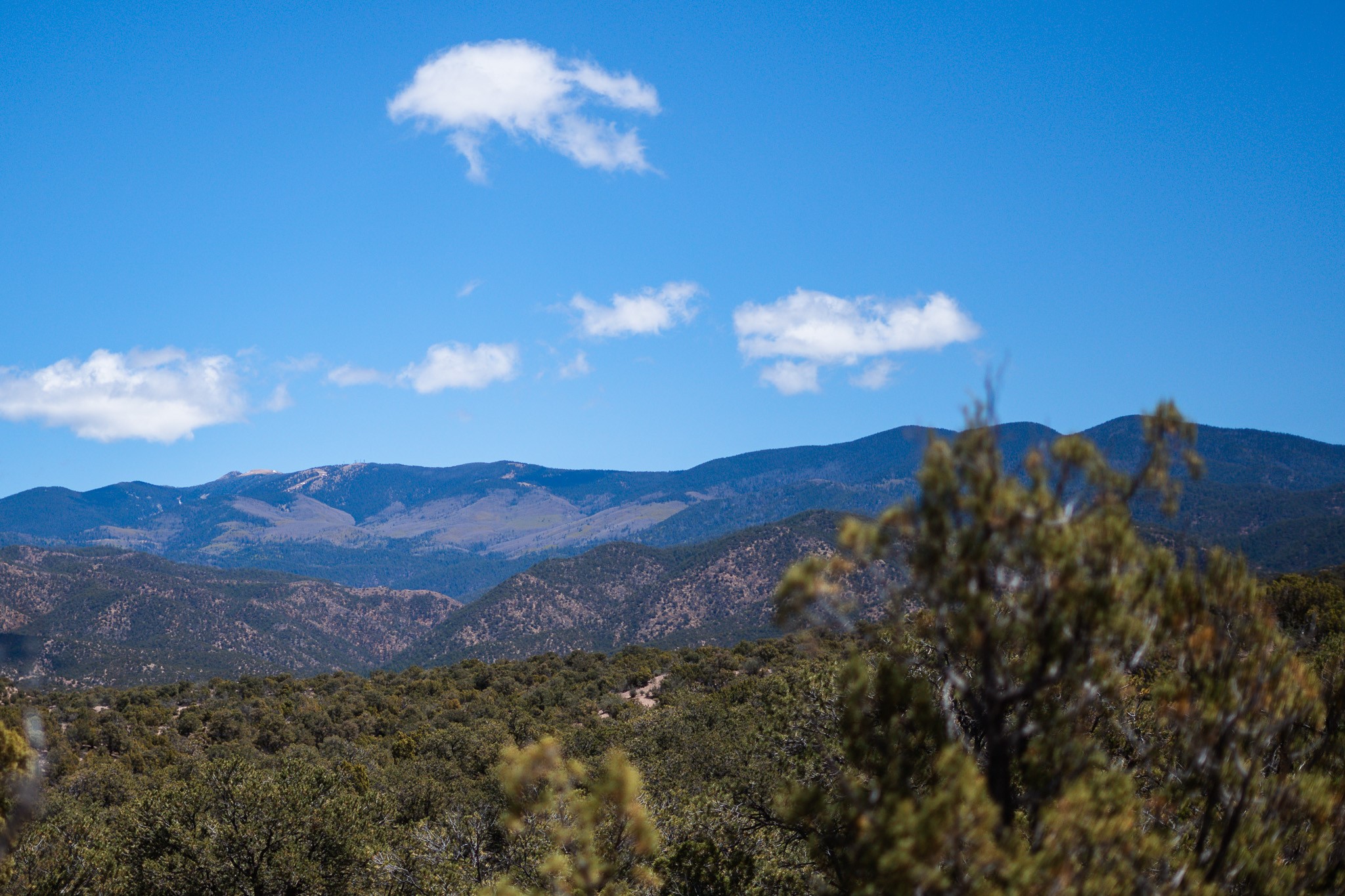 Scrub-covered land with layered mountain ridges beneath a blue, cloud-dotted sky.