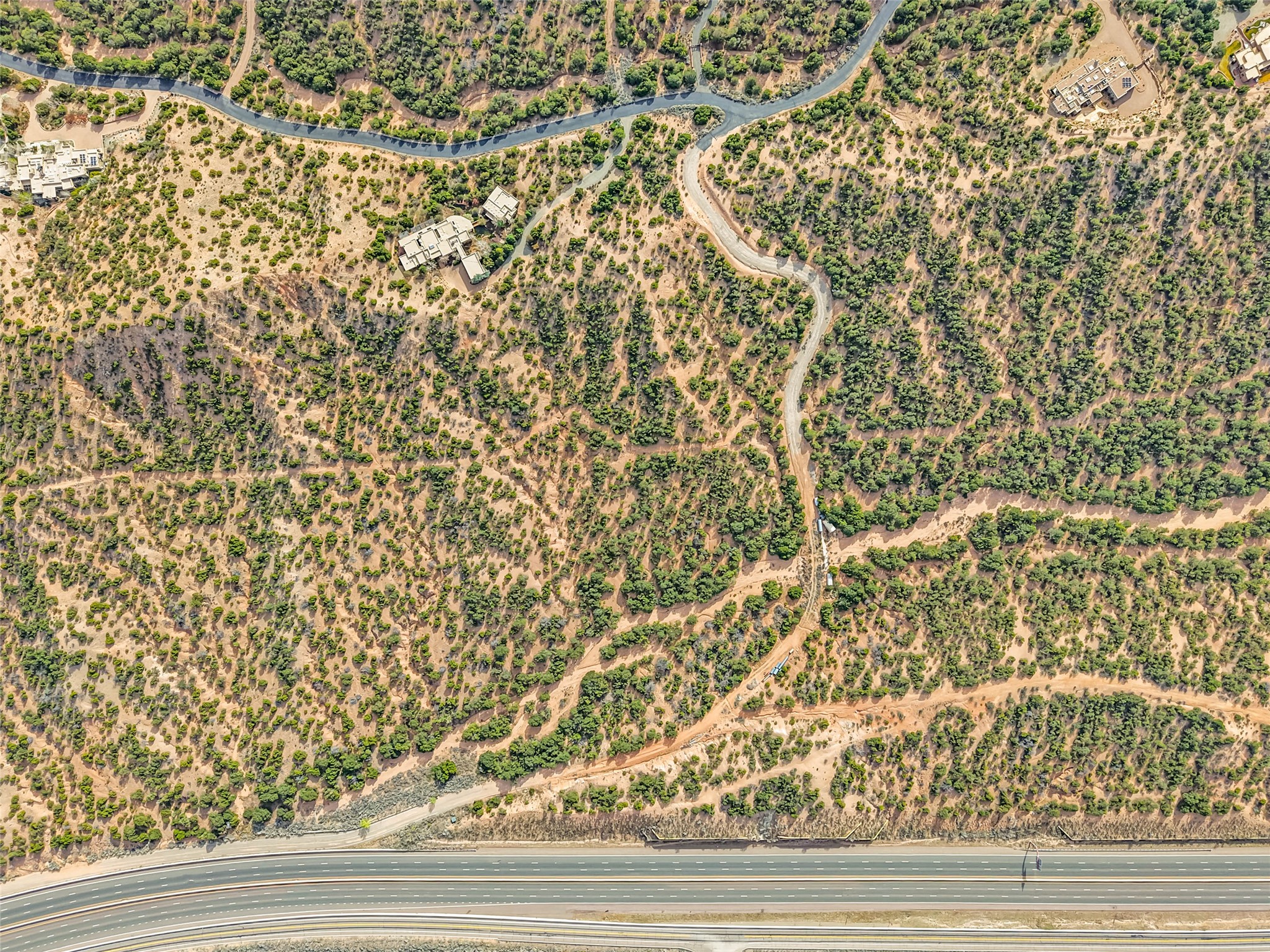 Aerial view of shrub-covered acreage with winding roads and a highway along its edge.