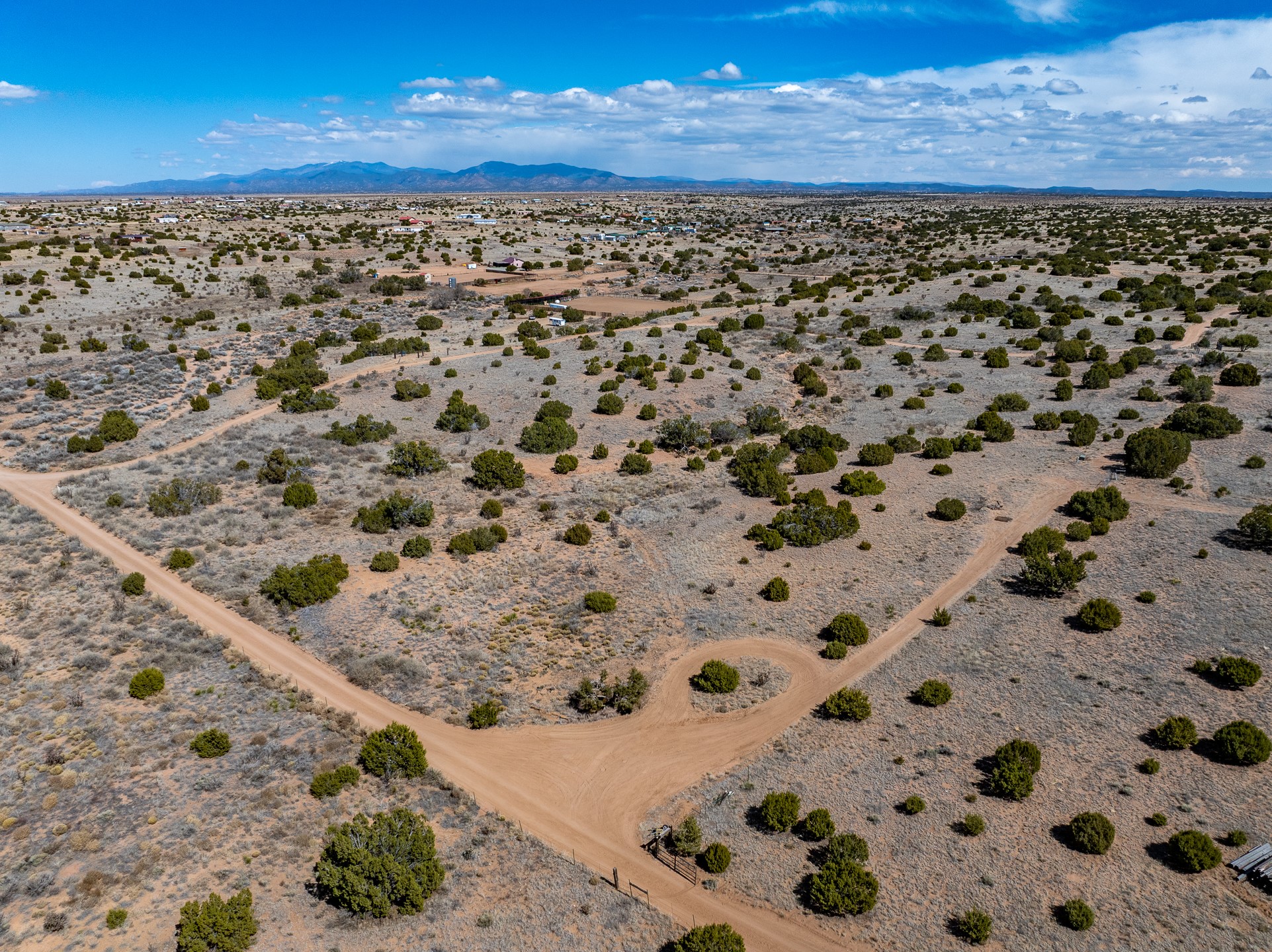 Aerial view of scrub-covered vacant land with dirt roads and distant mountains.