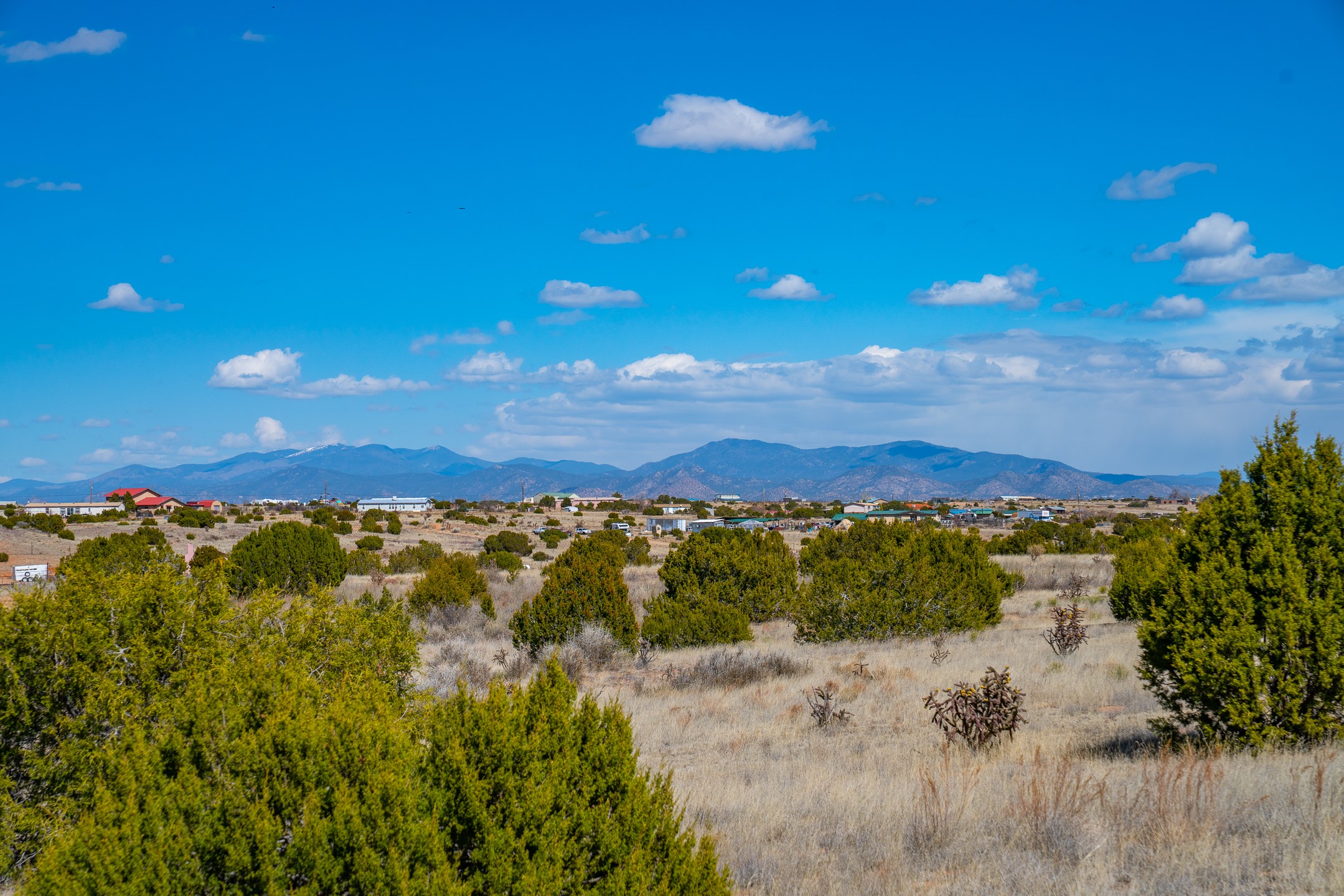 Vacant high-desert land with scattered shrubs and distant mountain views beneath a cloud-filled sky.