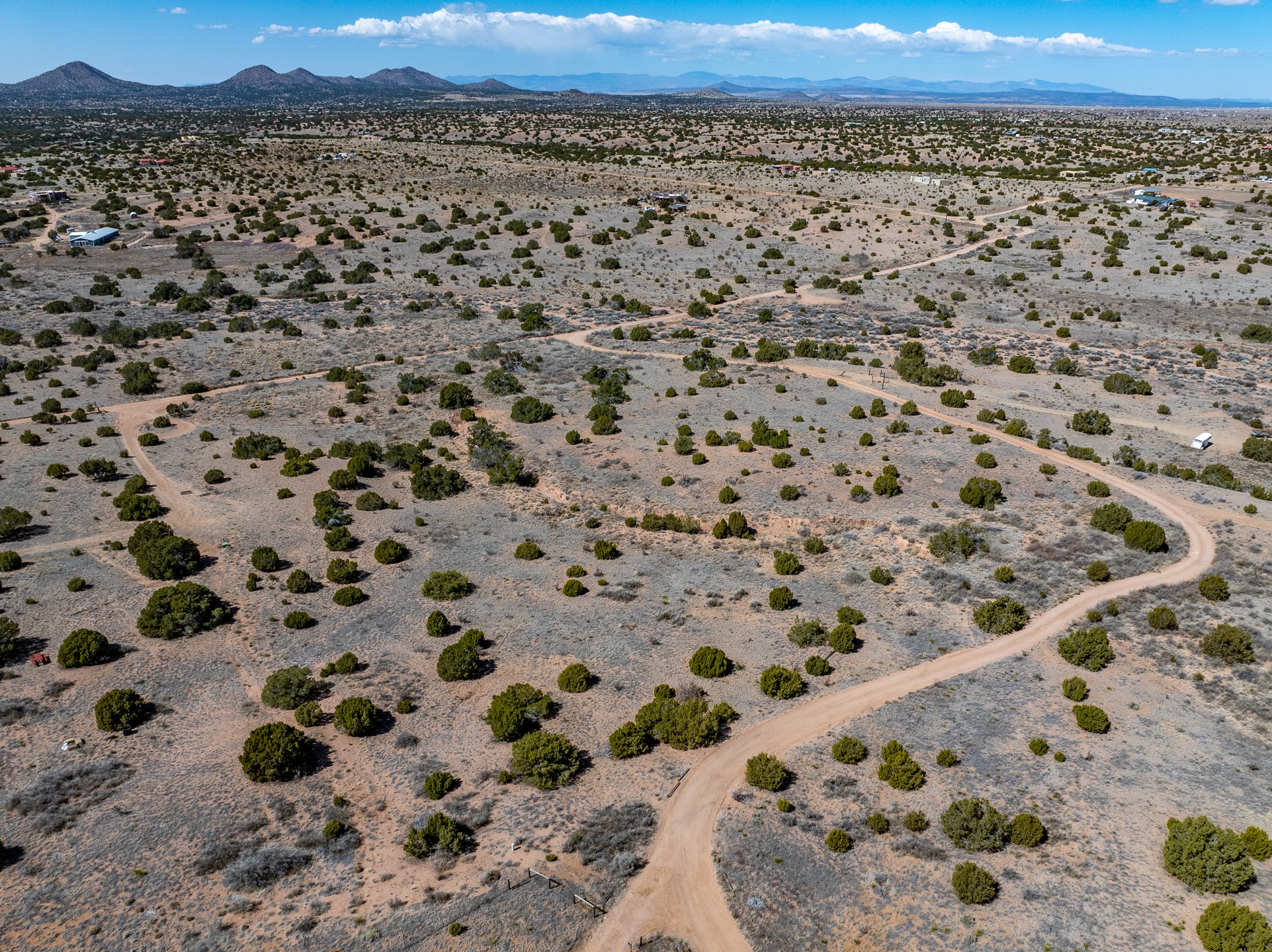 Aerial view of scrubland lots crossed by winding dirt roads, with distant mountains.