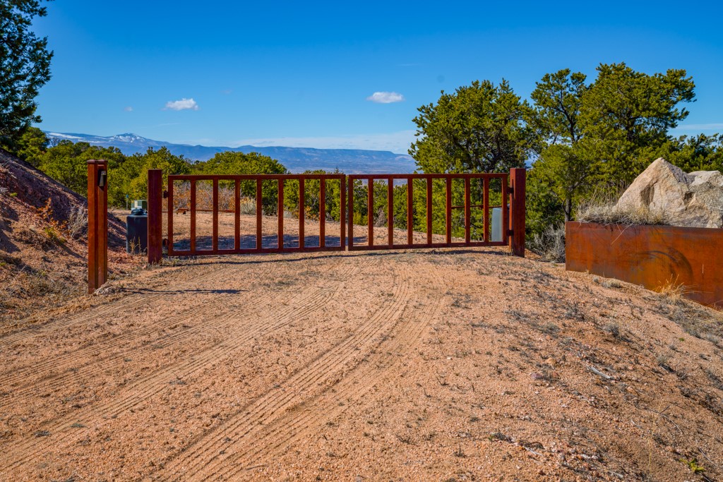 Dirt entrance to vacant land with a red gate and distant mountain views.