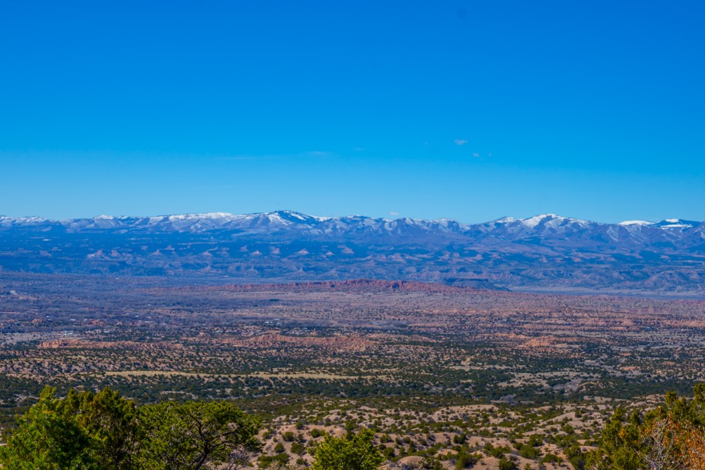 High-desert scrubland and scattered trees stretch toward a snow-dusted mountain range.