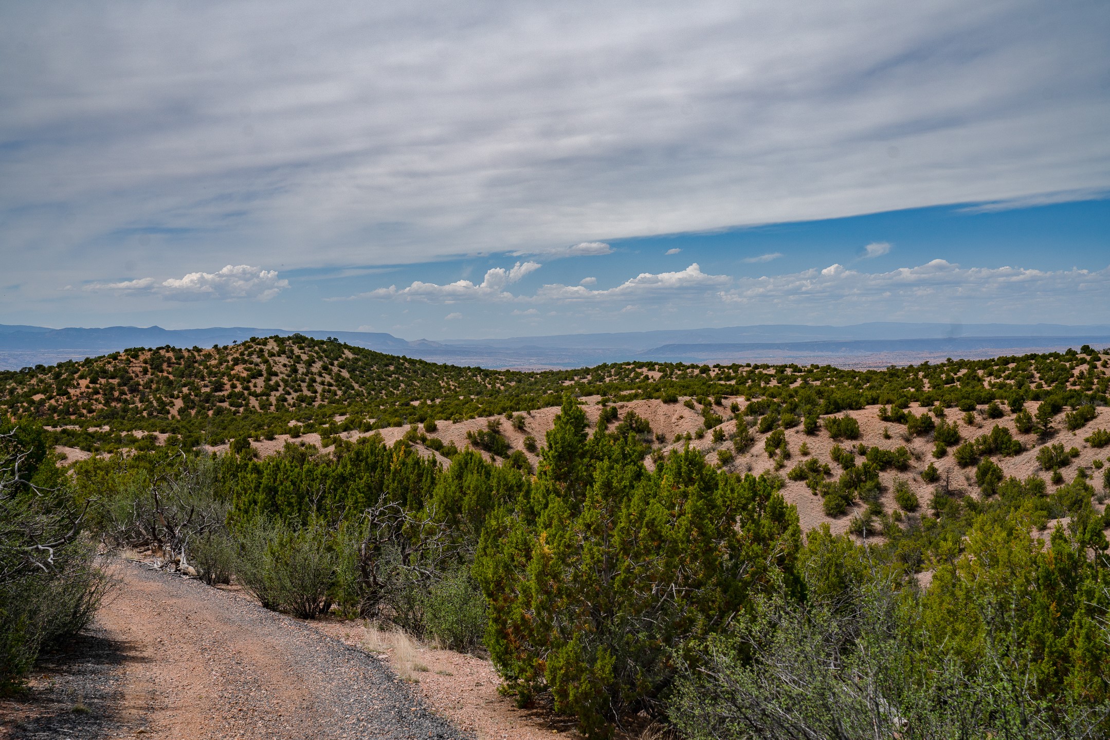 Shrub-covered hillside and dirt track overlooking distant mountain ranges.