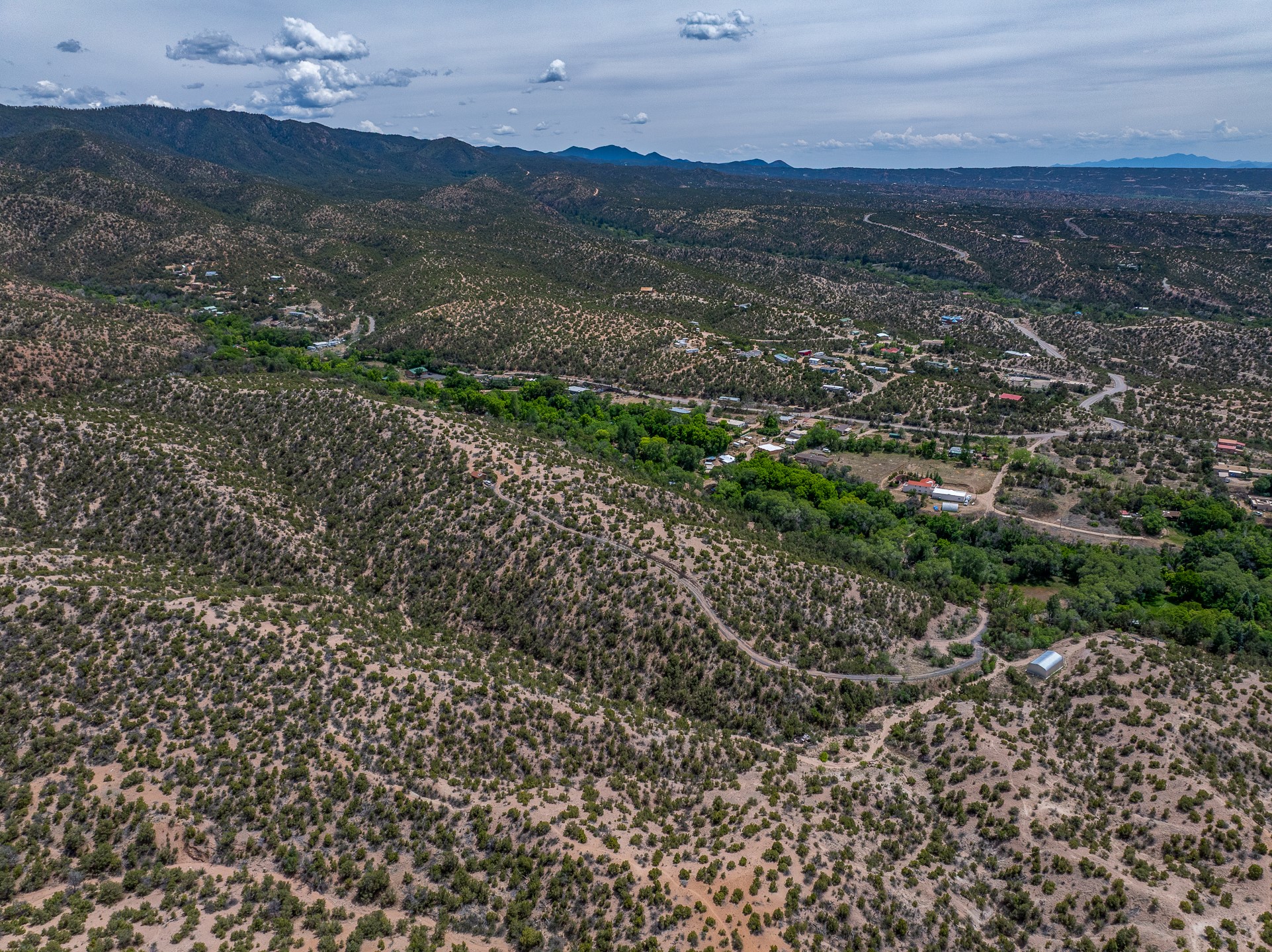 Aerial view of arid, shrub-covered terrain, scattered homes, winding roads, and distant mountain ridges.