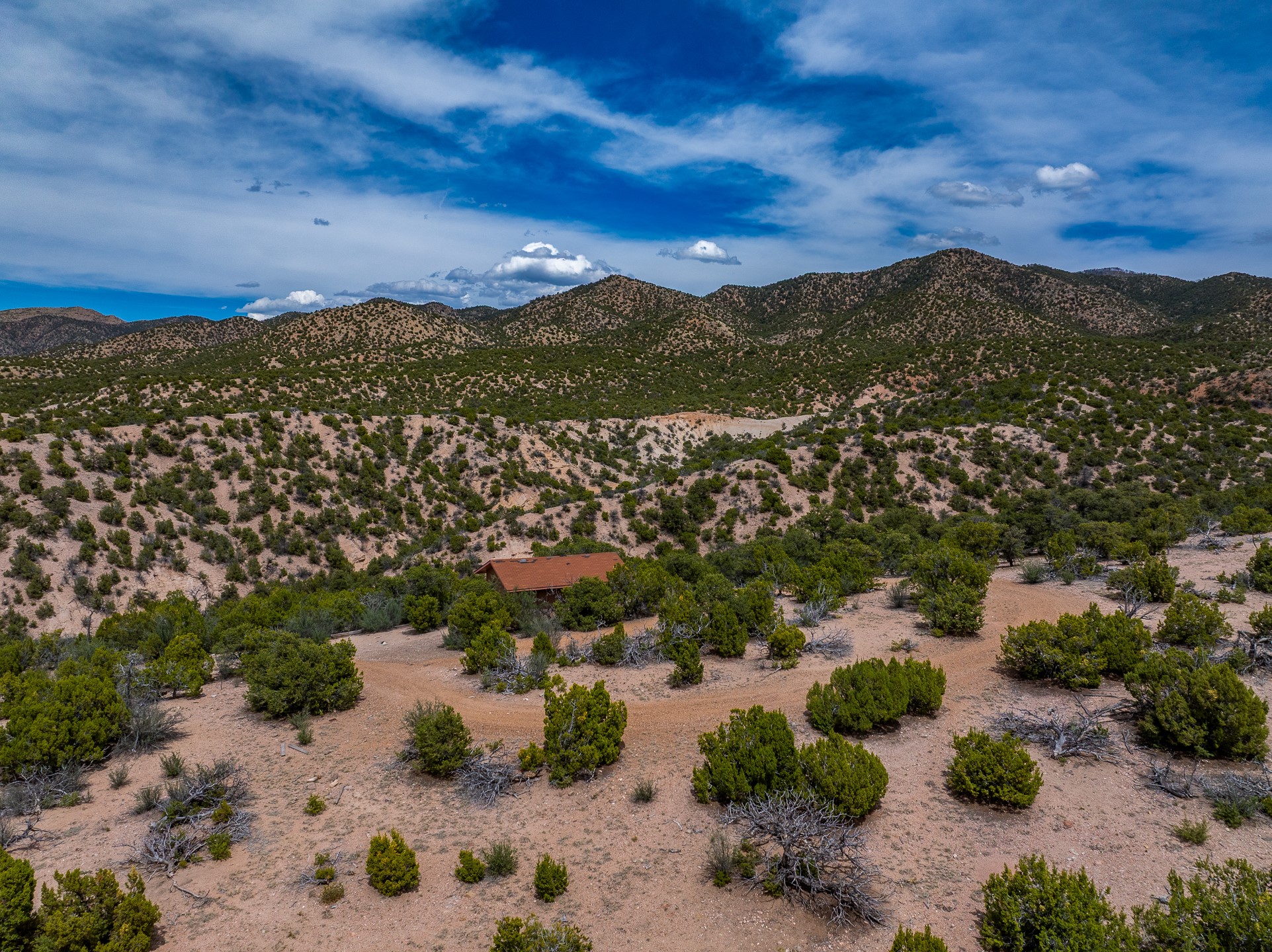 Aerial view of a scrub-covered property with a small red-roofed structure and mountains beyond.