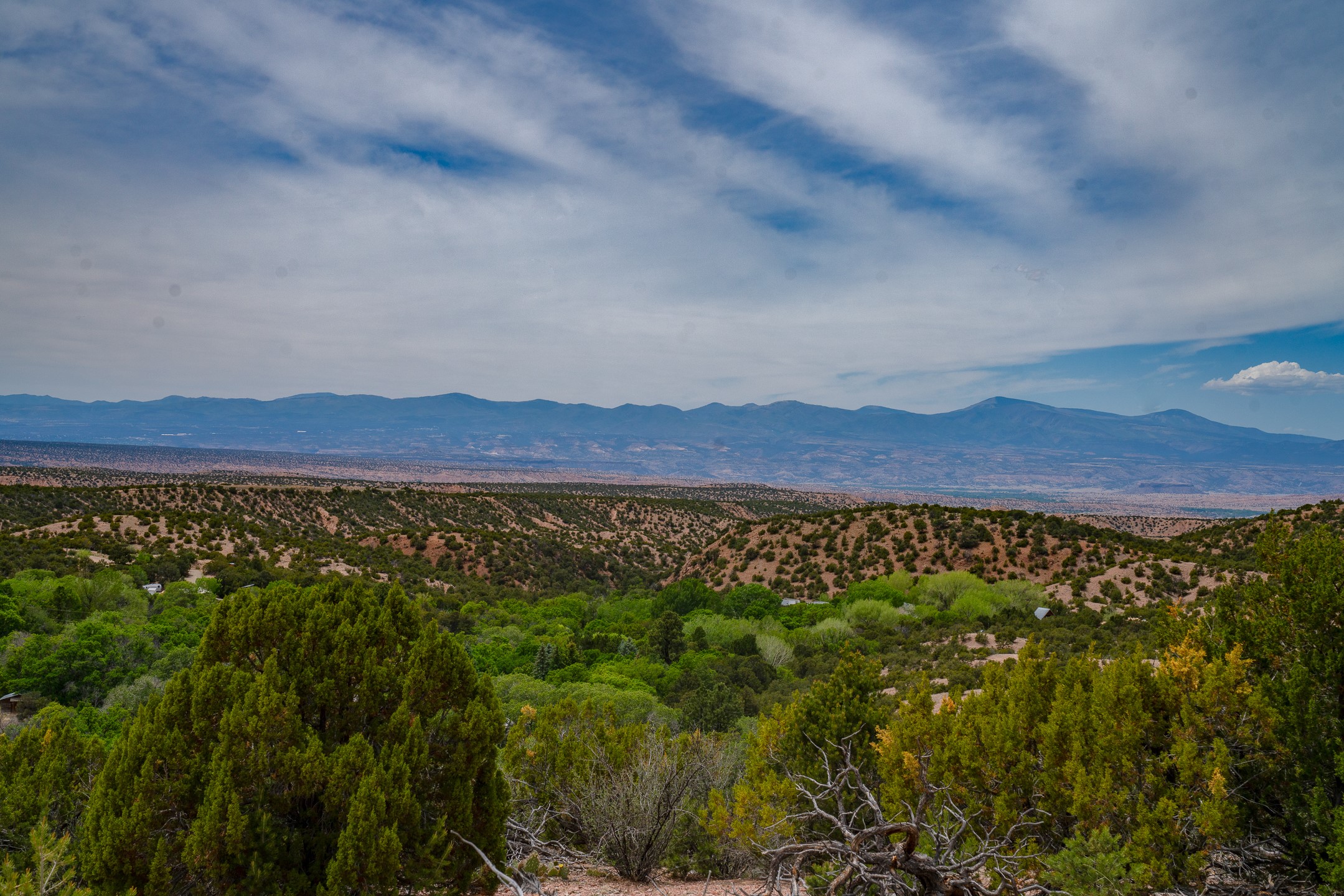 Panoramic mountain and valley view over wooded, arid hills beneath a cloudy blue sky.