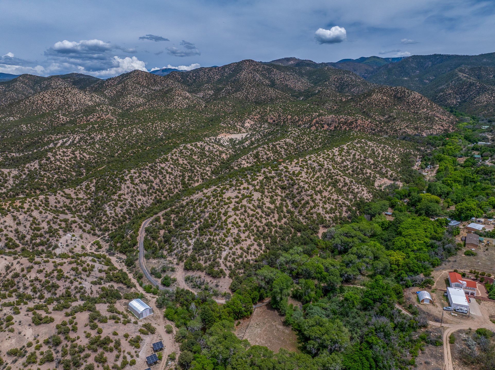 Aerial view of a rural property amid scrub-covered hills, with a winding road and mountain ranges beyond.