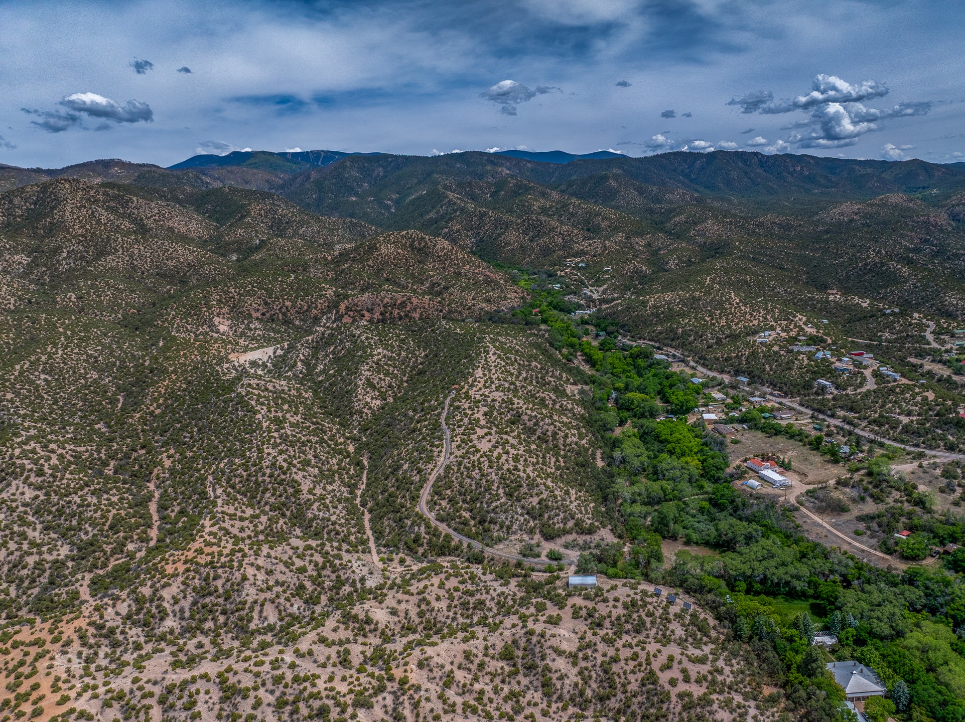 Aerial view of scrub-covered hills, scattered homes, and a green valley with mountains in the distance.