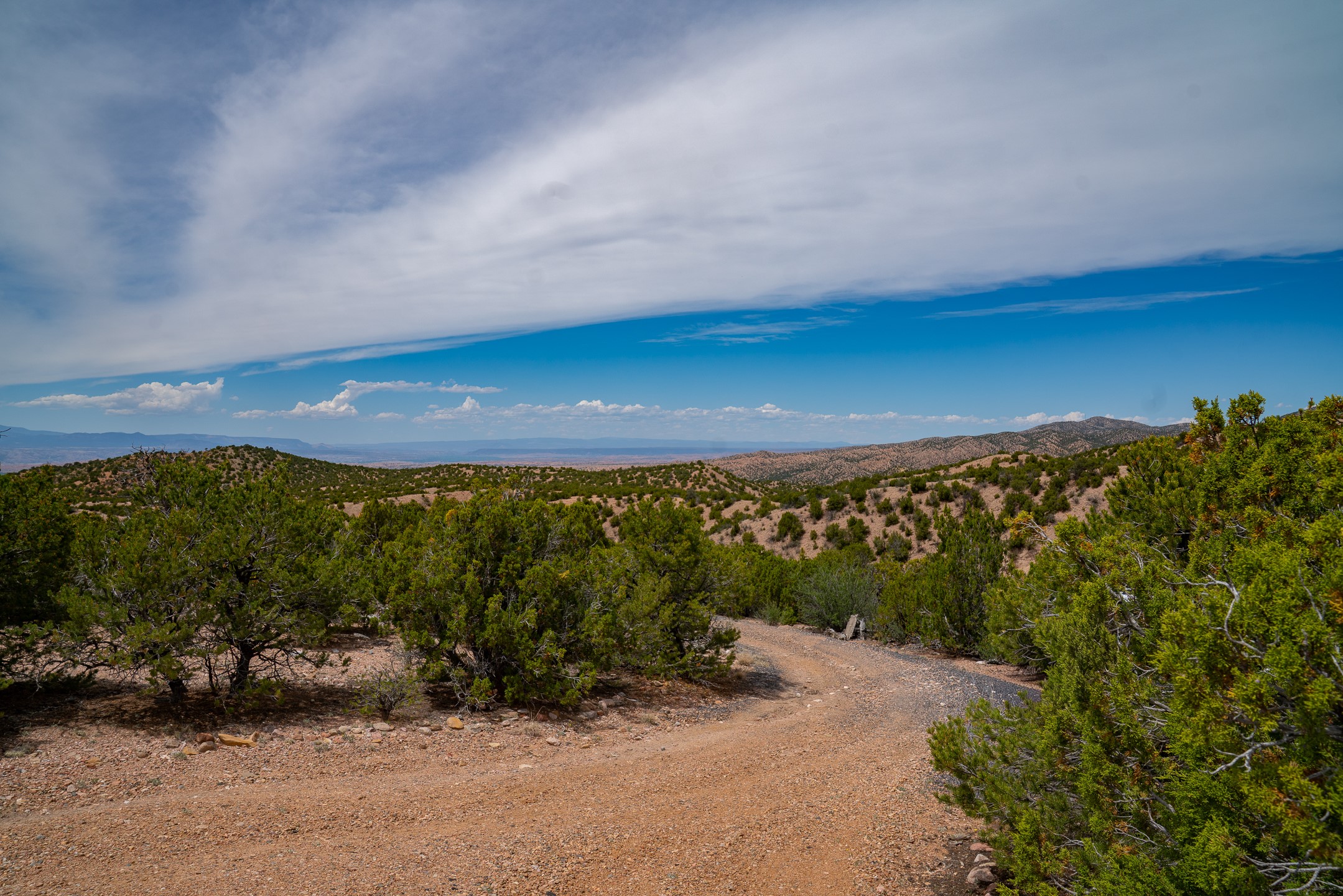 Dirt road winds through juniper-covered hills with distant mountain views.