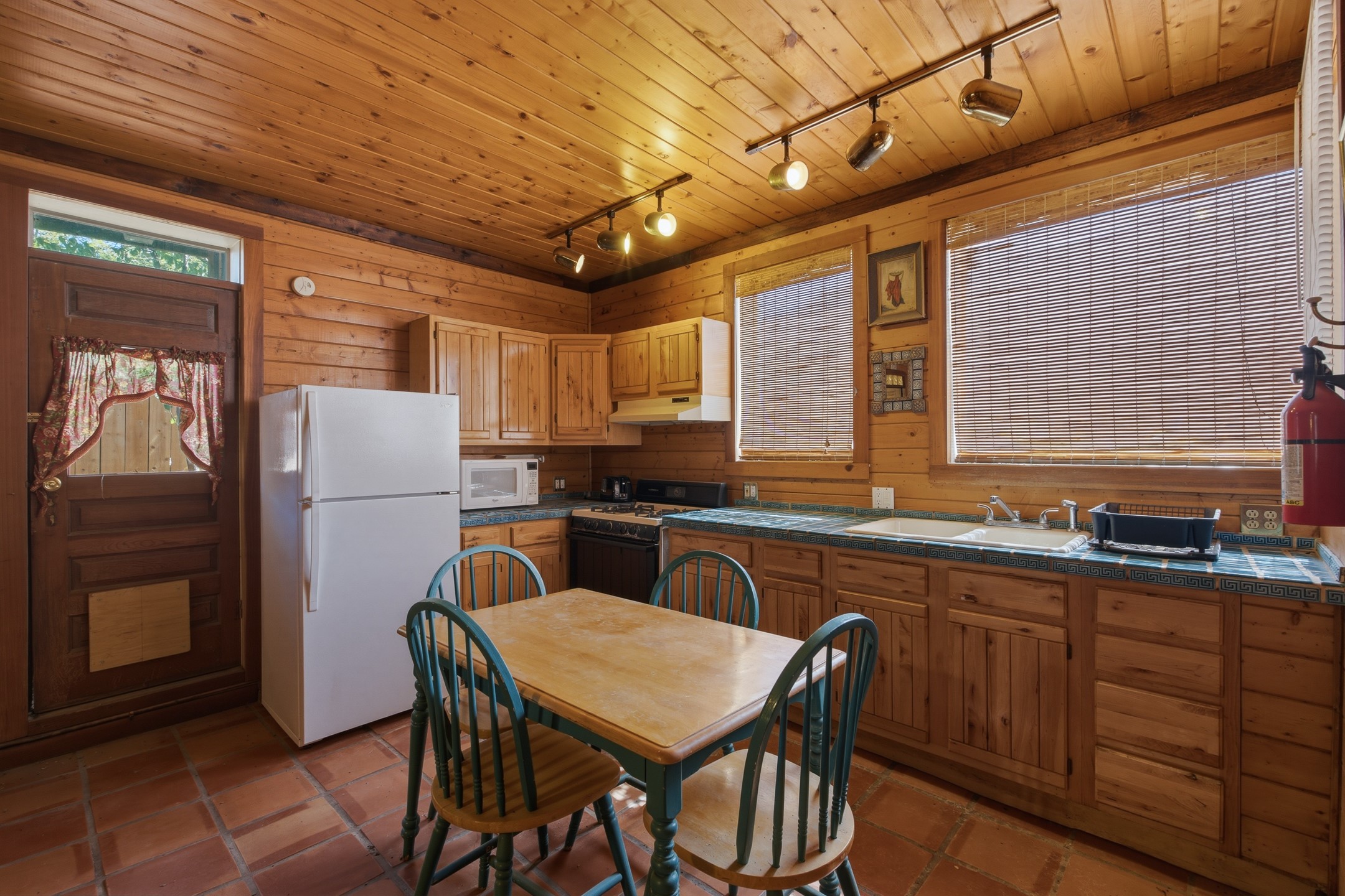 Wood-paneled kitchen with blue tile countertops, terracotta floors, and a small dining table.