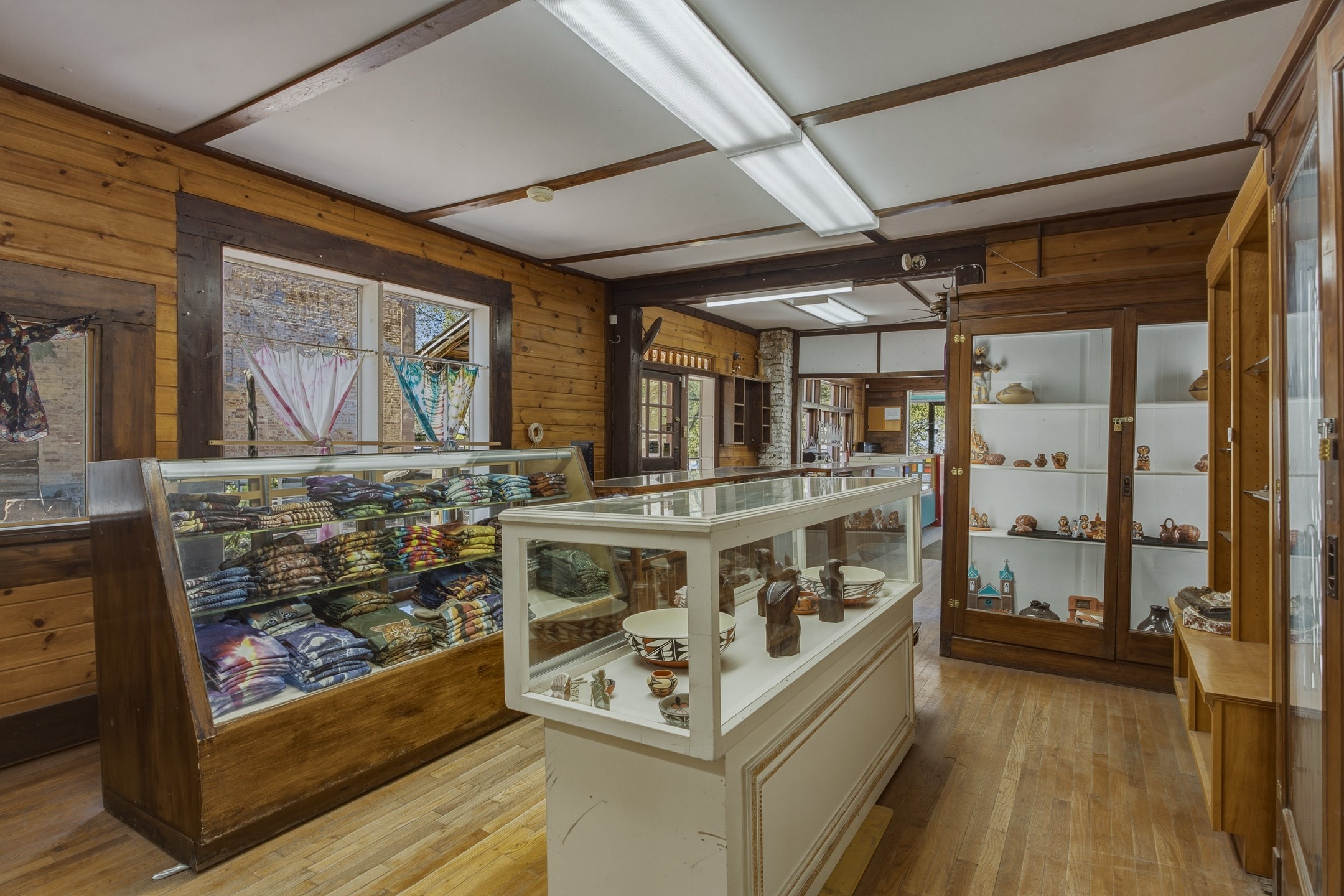 Rustic shop interior with glass cases displaying folded textiles and pottery.