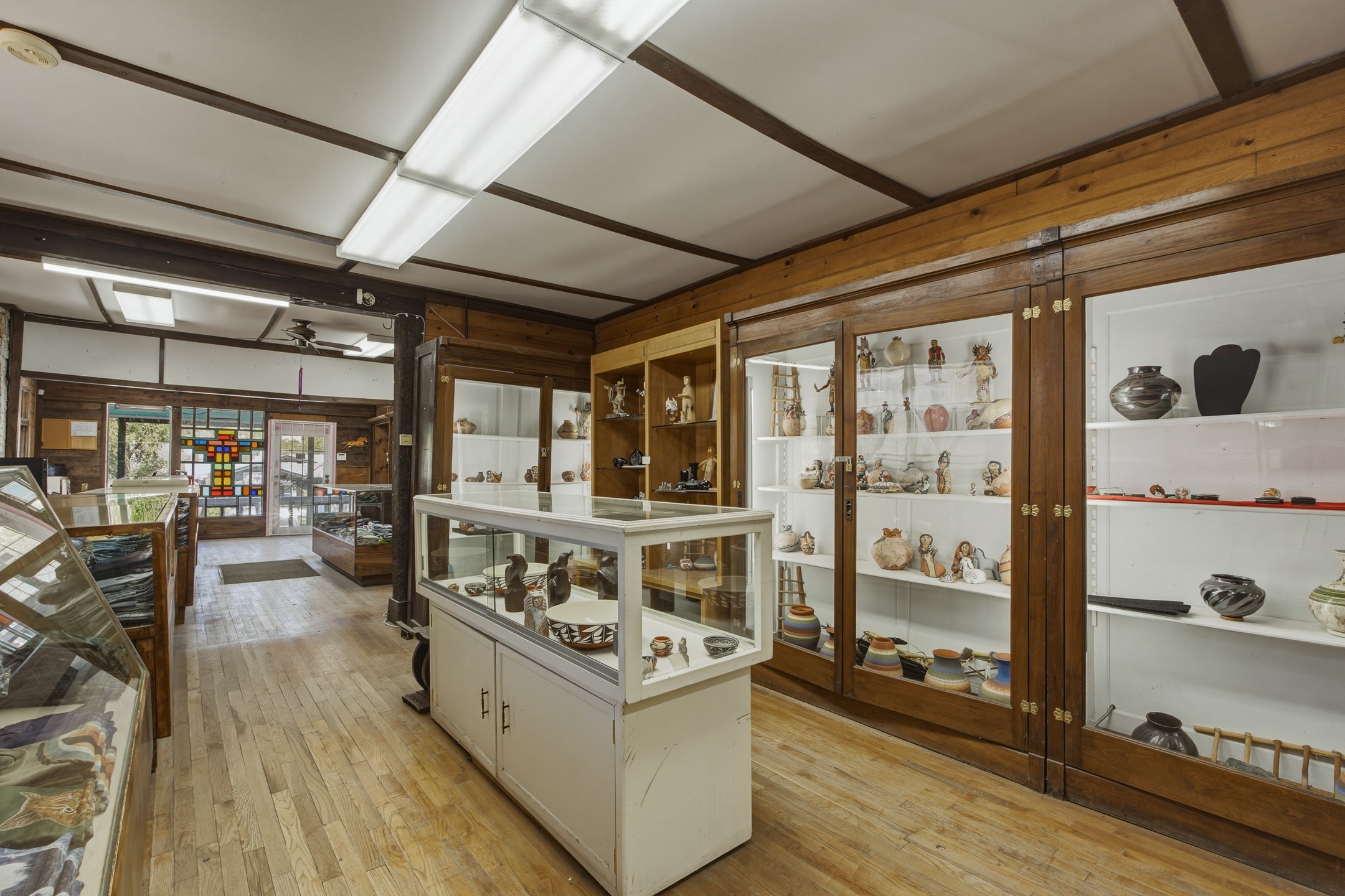Retail shop interior with wood floors, pottery-filled display cabinets, and a colorful stained-glass panel by the entrance.