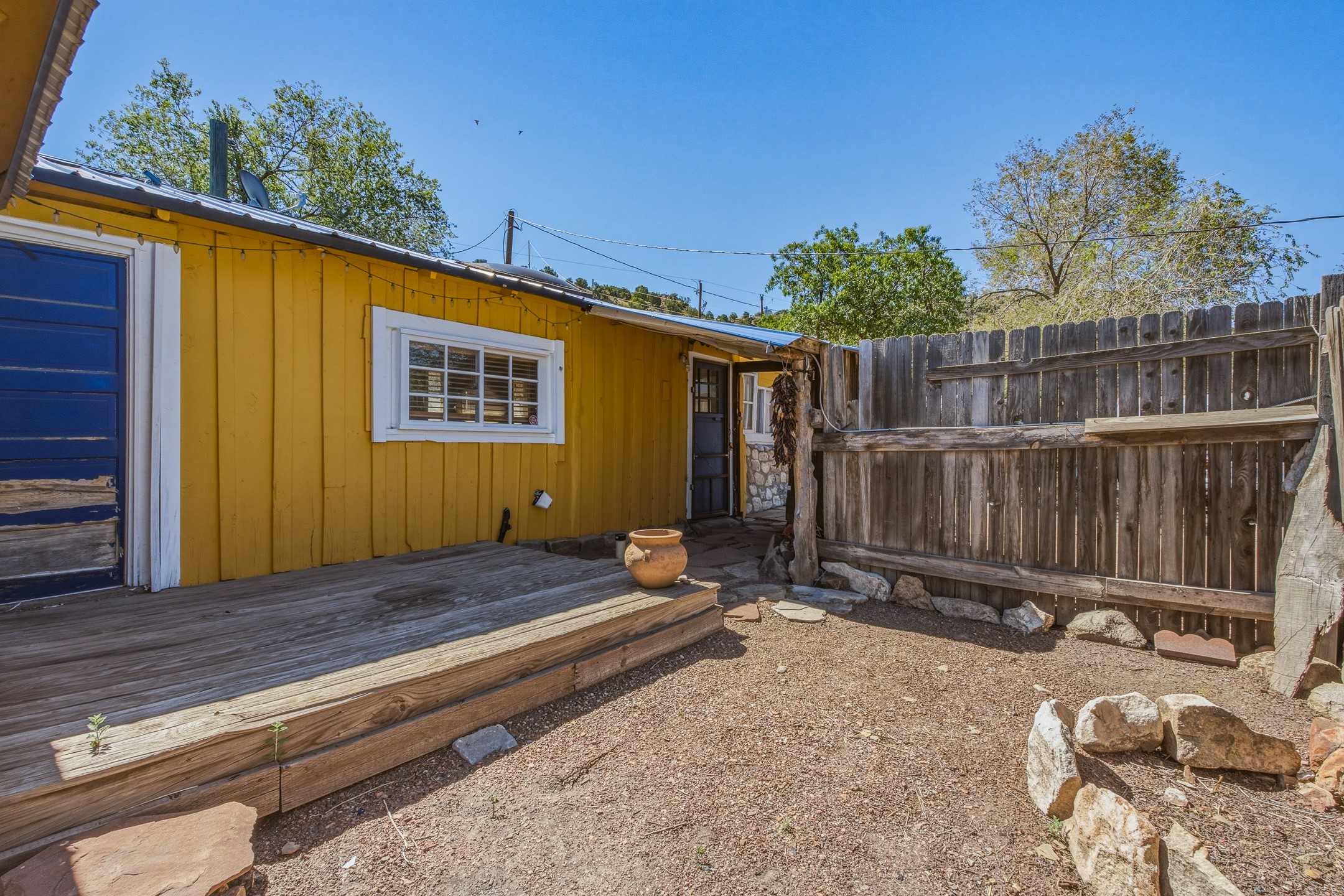 Yellow-sided home with a weathered wood deck beside a fenced gravel yard and terracotta planter.
